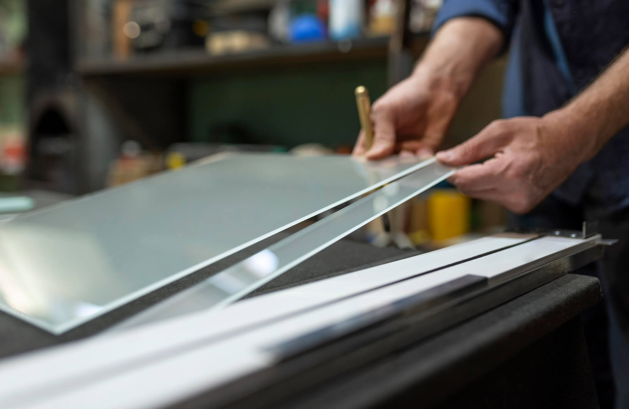Hands of a worker measuring and preparing glass panels for mirror production, showing precision tools and reflective surfaces.