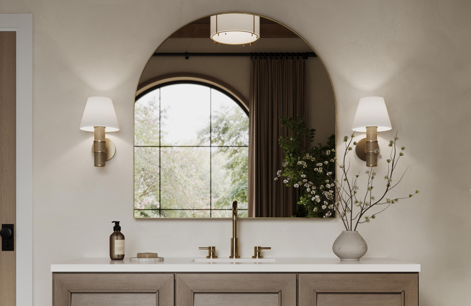 Modern vanity setup featuring an arched mirror framed in brass, paired with white-shaded sconces and minimalist brass faucet hardware.