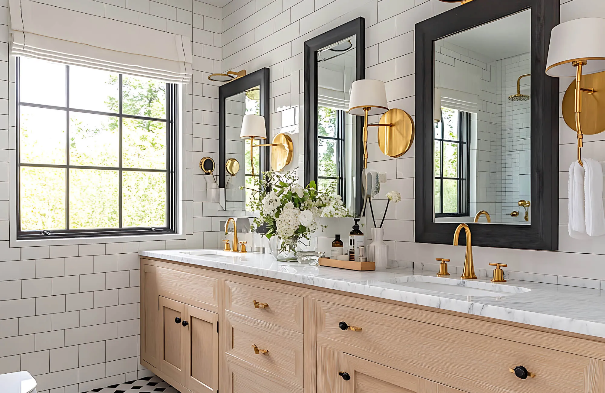 Bright and elegant bathroom with double vanity, gold fixtures, white subway tiles, and wall sconces beside framed mirrors.