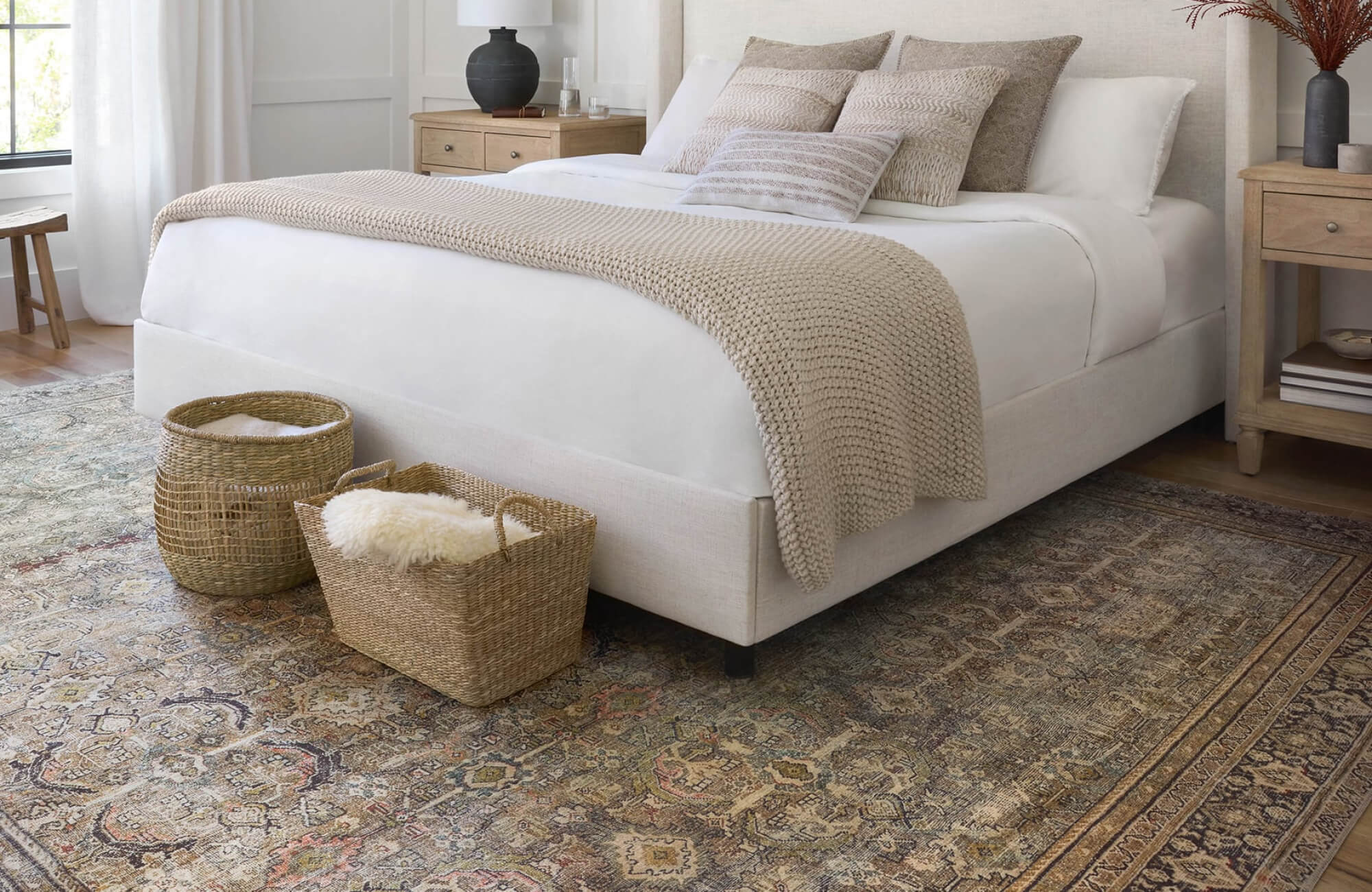Serene bedroom with neutral bedding and a vintage-style rug in muted earth tones, adding warmth and texture underfoot.
