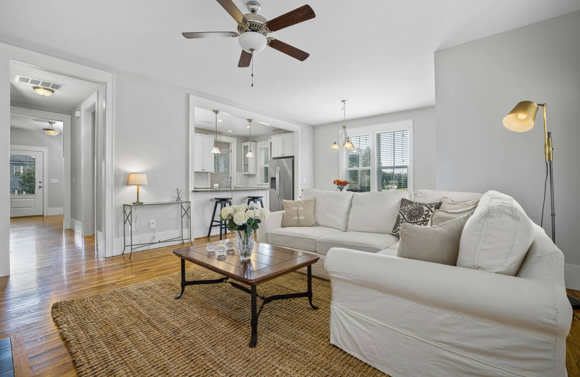 Bright open-concept living room with a woven jute rug grounding a white sectional sofa and warm wood floors.