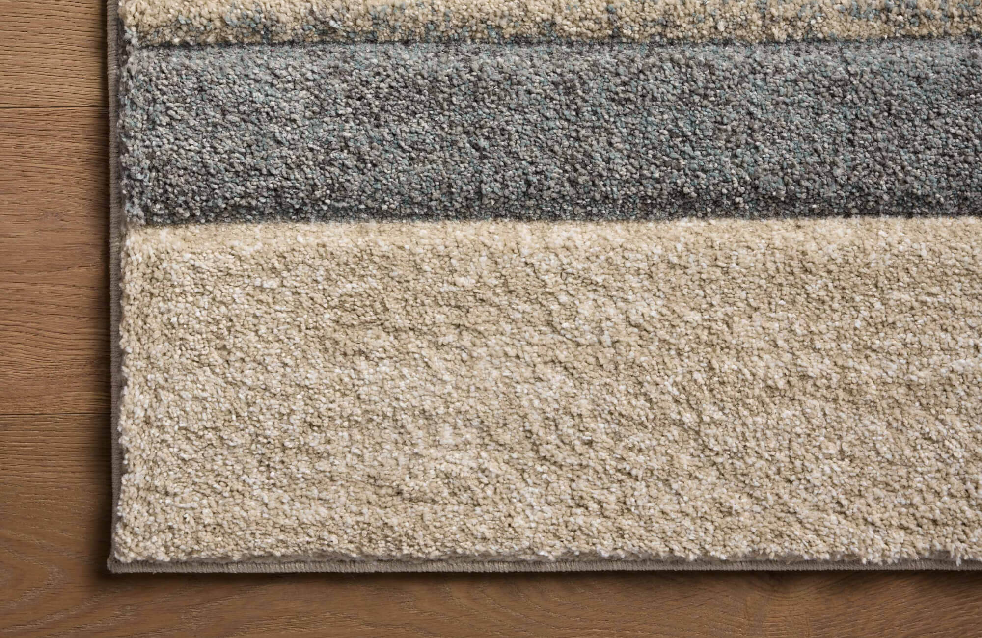 null Textured area rug with horizontal bands of cream, taupe, and gray, styled over natural oak flooring for a calm, space-friendly palette.