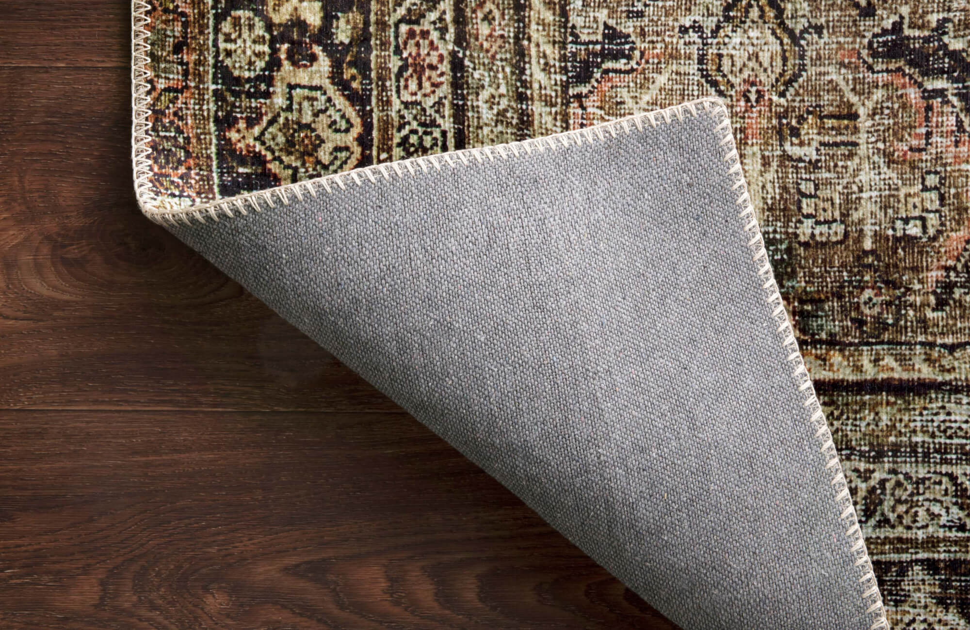 null Corner of a vintage-style rug flipped to reveal its non-slip gray backing, shown on dark wood flooring to highlight its secure and durable construction.