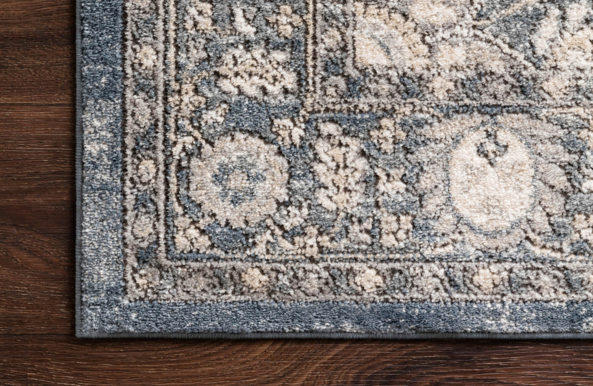 null Textured wool-blend rug in soft blue and cream tones, featuring a subtle vintage pattern and thick edging, shown over dark hardwood for contrast.