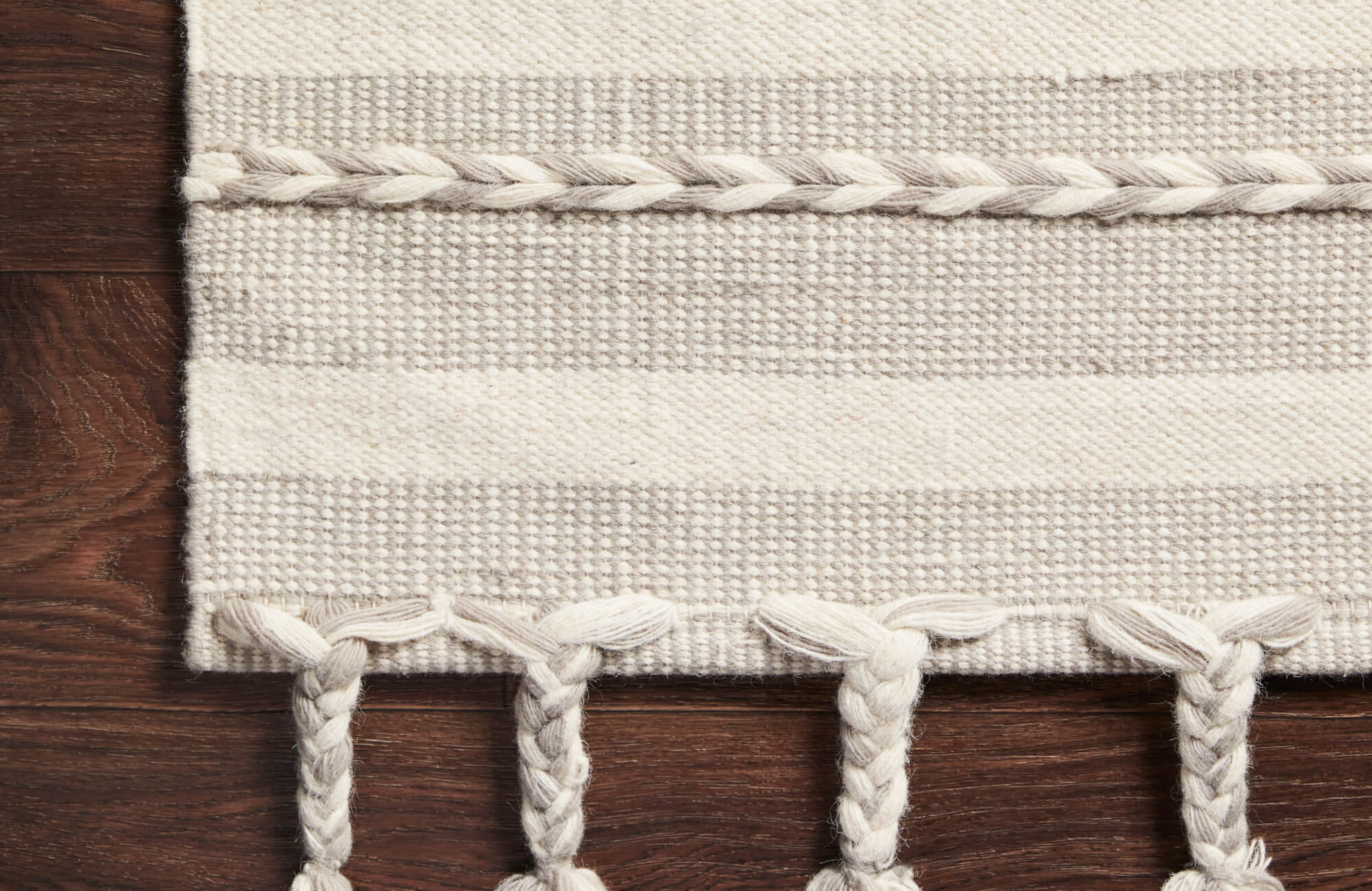 null Neutral-toned rug with thick woven stripes and knotted fringe tassels, offering a soft, organic touch against deep brown hardwood floors.