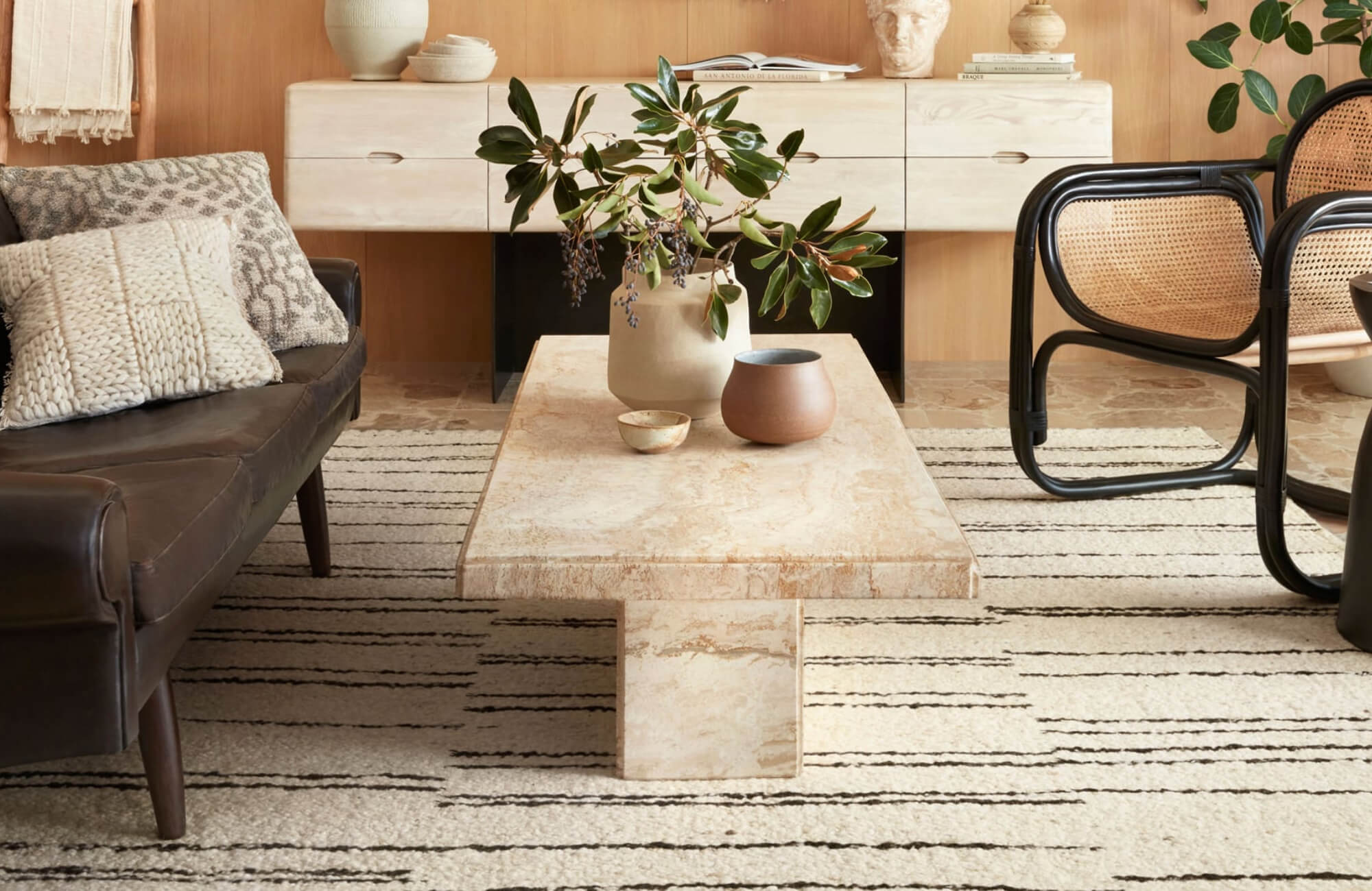 null Neutral-toned living room with a cream and black striped rug, stone coffee table, and mixed seating that creates a clean, airy layout in a compact space.