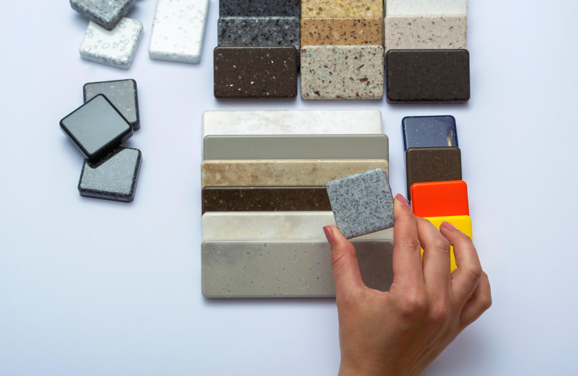 null Hand holding a gray tile sample above an assortment of stone and ceramic surface swatches in various colors and textures on a white background.