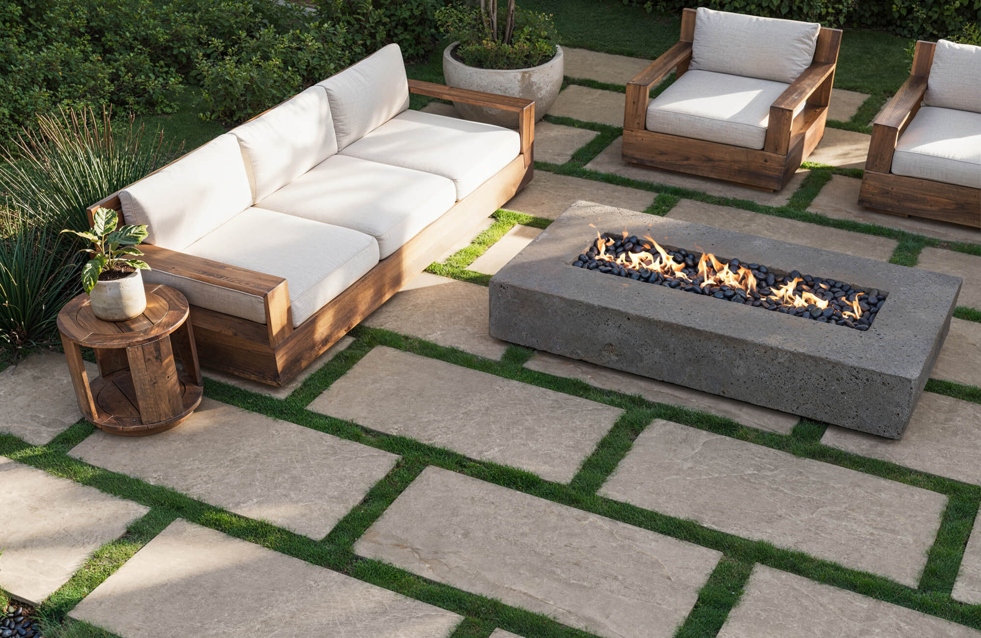 Contemporary backyard with light porcelain pavers and a concrete fire feature, styled with natural wood furniture and greenery.