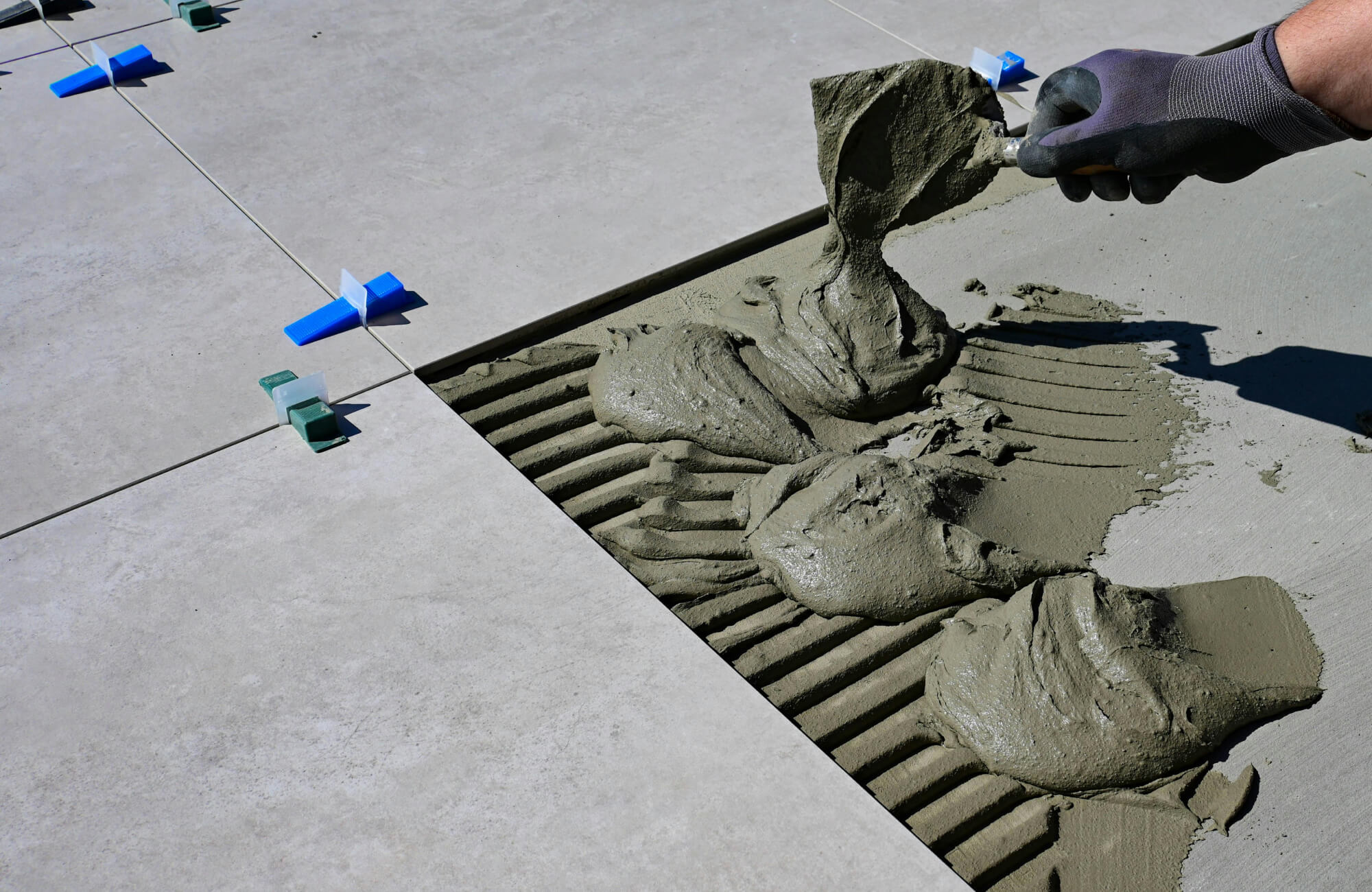 Outdoor porcelain tile is being installed with notched mortar lines and leveling spacers for precise placement.