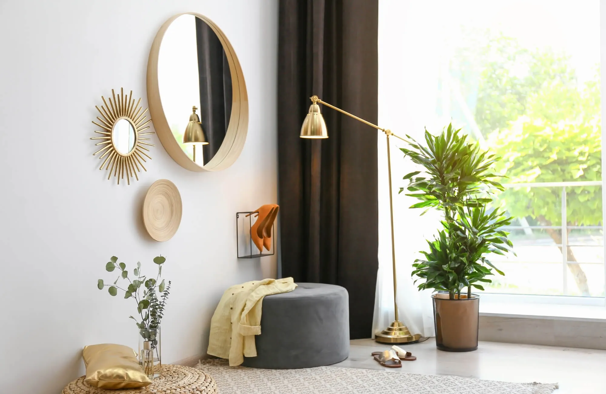 Modern living room corner with round and sunburst mirrors, gold floor lamp, potted plant, and cozy seating accents.
