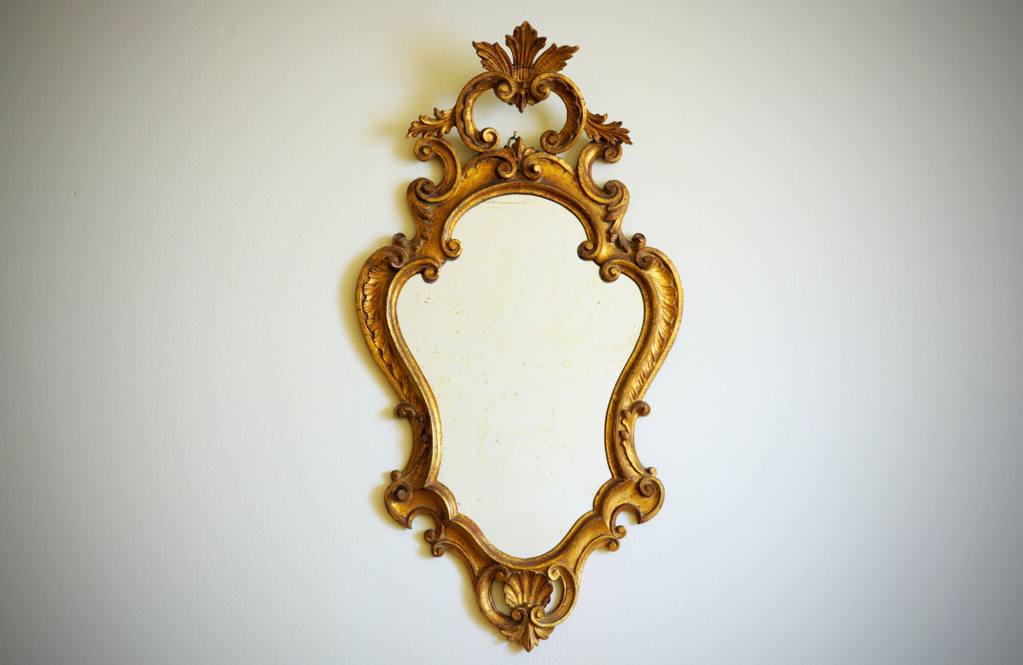 null Antique gold ornate wall mirror with intricate scrollwork and leaf details, displayed against a plain off-white background.