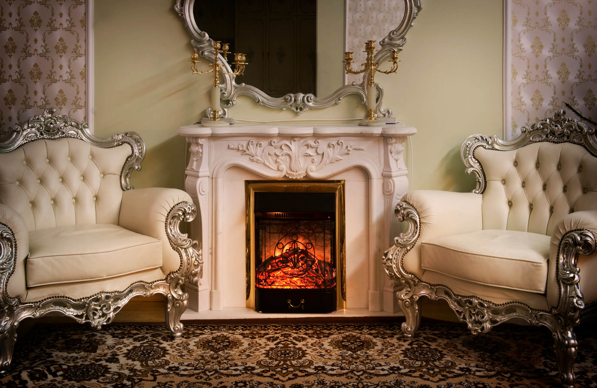 null Luxurious living room with ornate silver-framed chairs, white carved fireplace, gold candelabras, and decorative wall mirror.