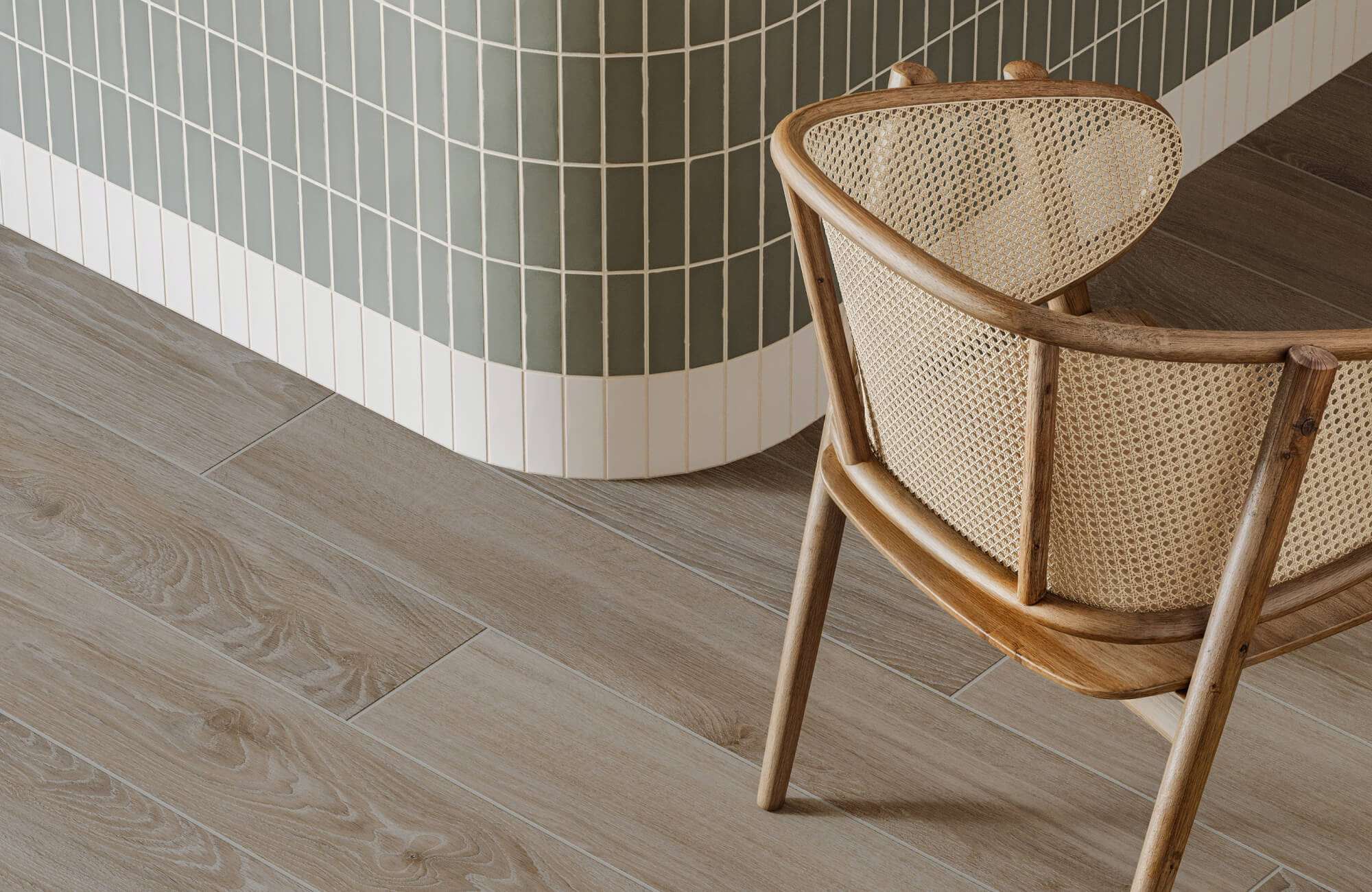 null Light wood look tile flooring with soft oak-style grain runs beside a curved wall of vertical green and white tile, paired with a woven cane chair in a warm natural wood frame.