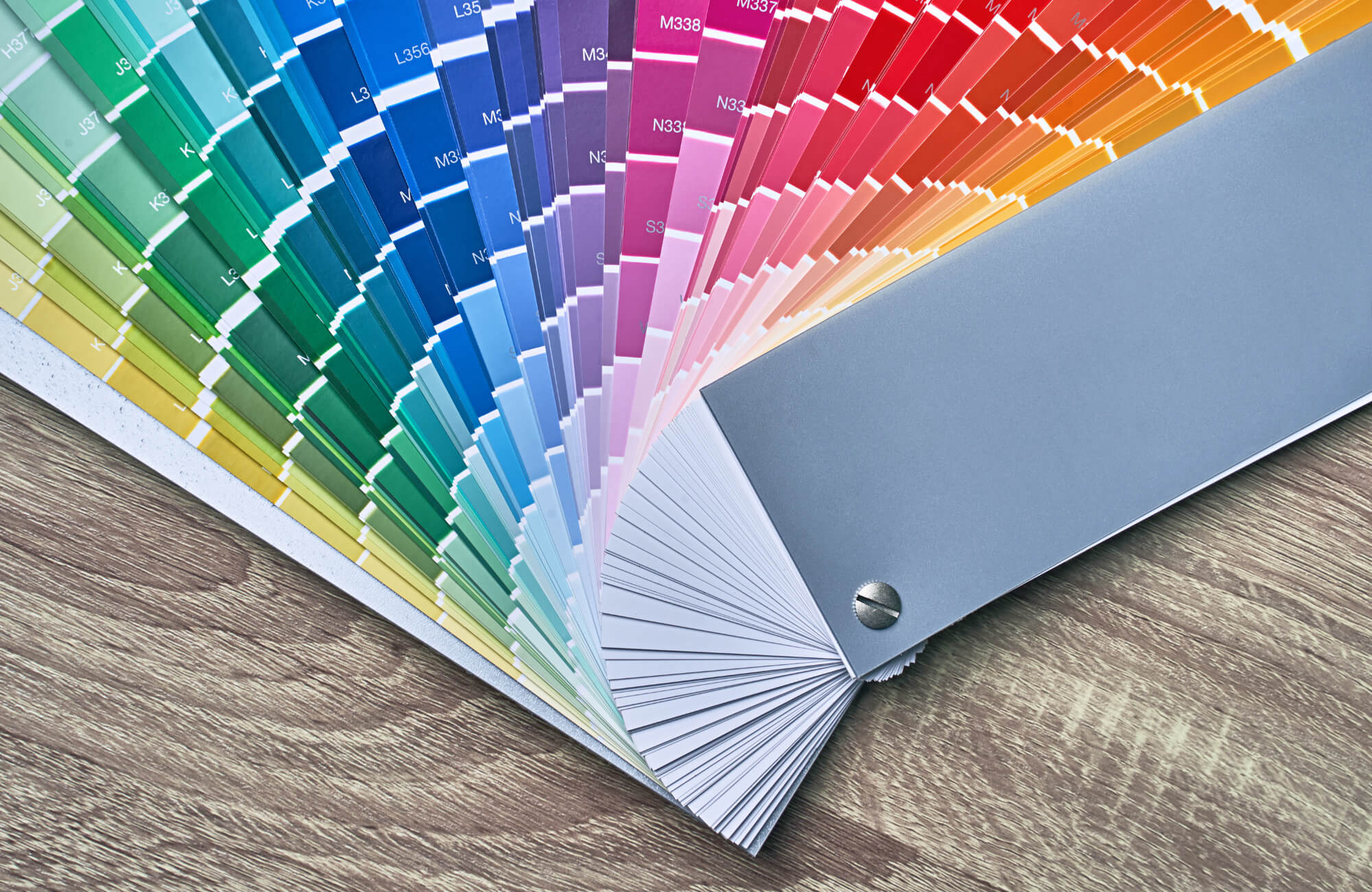 null Fan deck of color swatches arranged in a gradient spectrum from green to red, displayed on a wood surface for color matching reference.