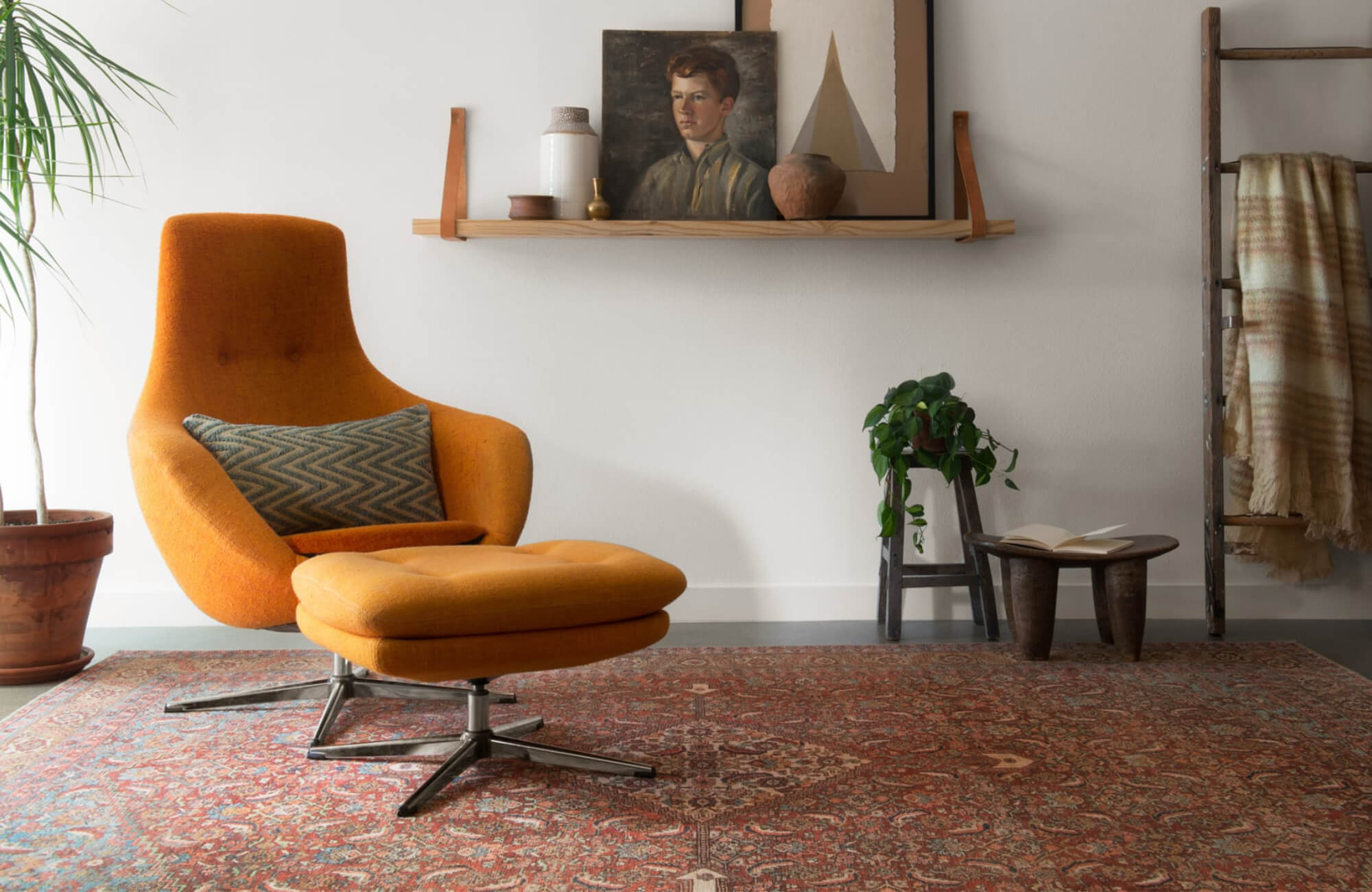 null Cozy reading corner with an orange lounge chair, red patterned rug, wooden decor accents, and a shelf displaying artwork and pottery.