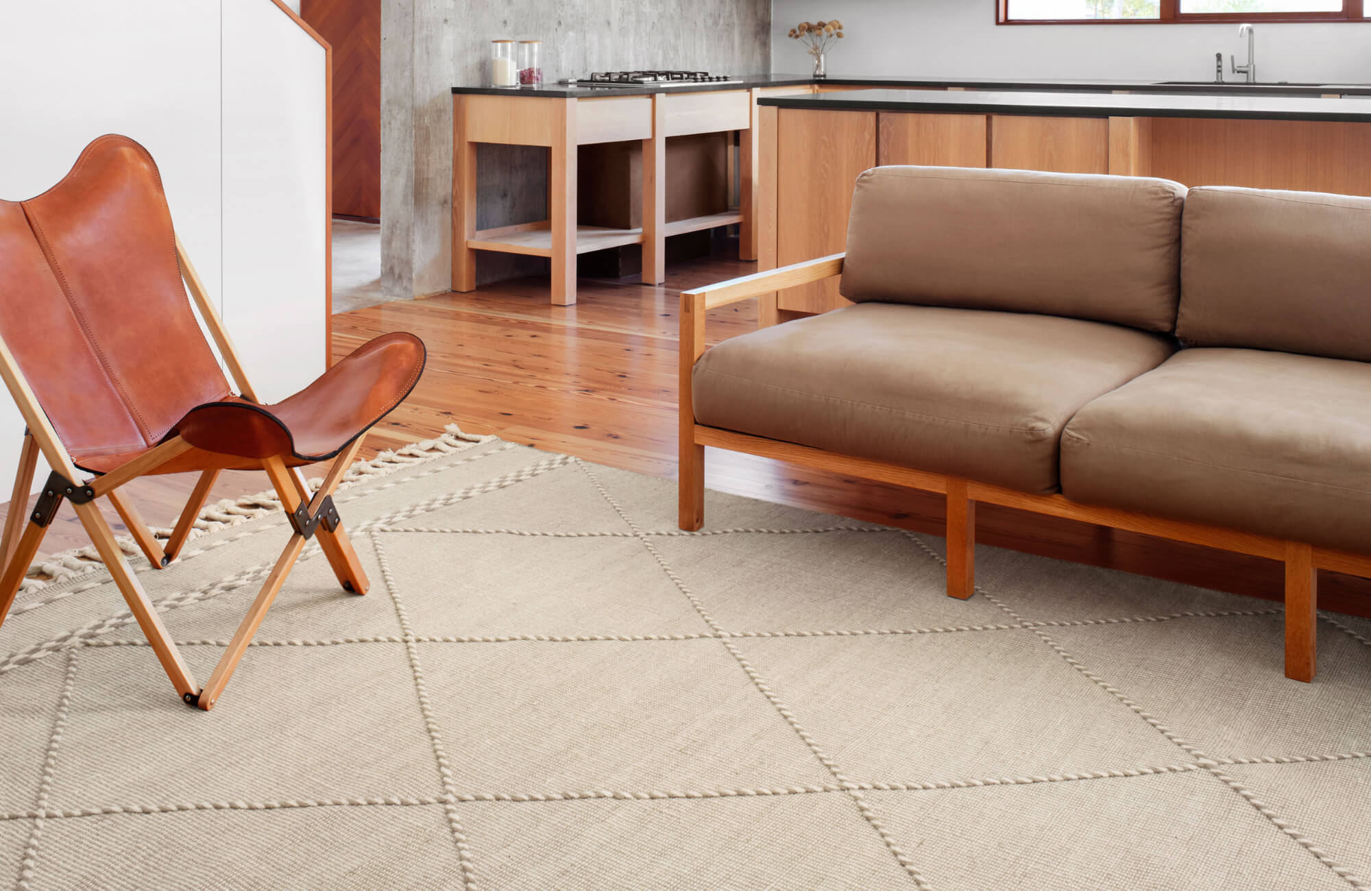null Modern open-concept space with a tan leather sofa, wood-framed butterfly chair, and a cream diamond-patterned rug over hardwood floors.