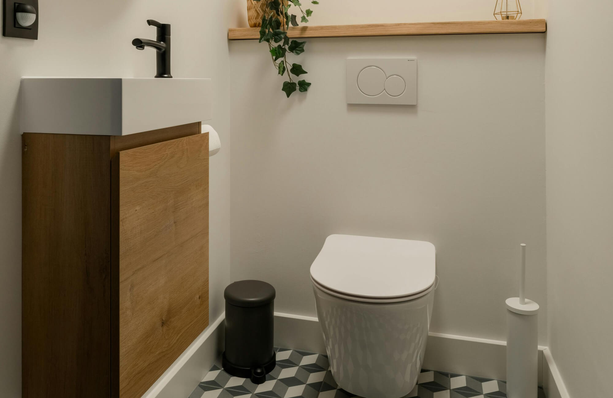 null Minimalist WC with geometric floor tiles, wall-mounted wood vanity, matte black tap, and modern dual-flush toilet.