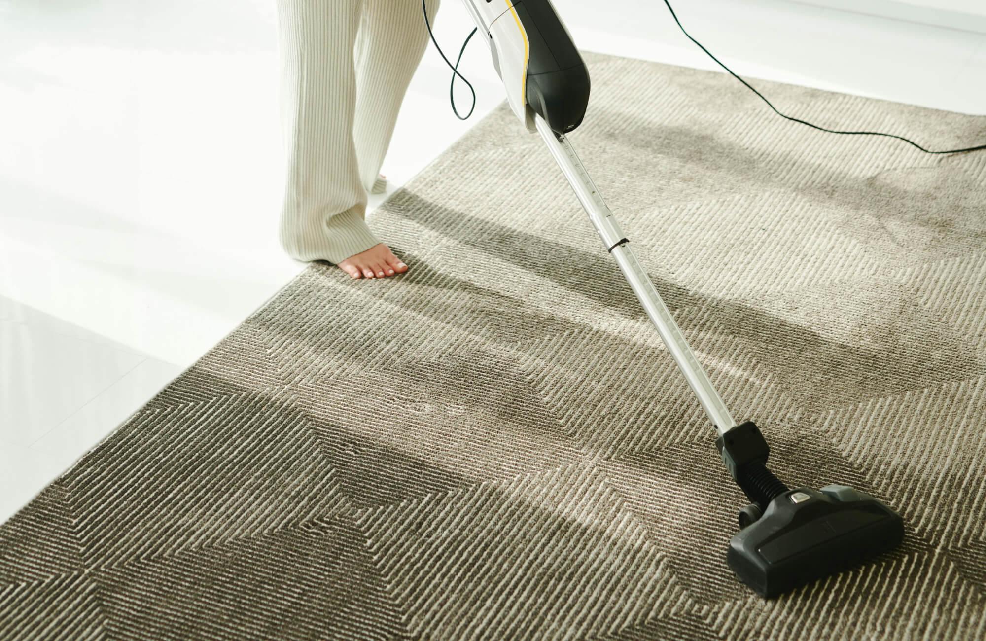 null Person vacuuming a polypropylene area rug with a modern geometric pattern in neutral tones, enhancing a clean and stylish space.