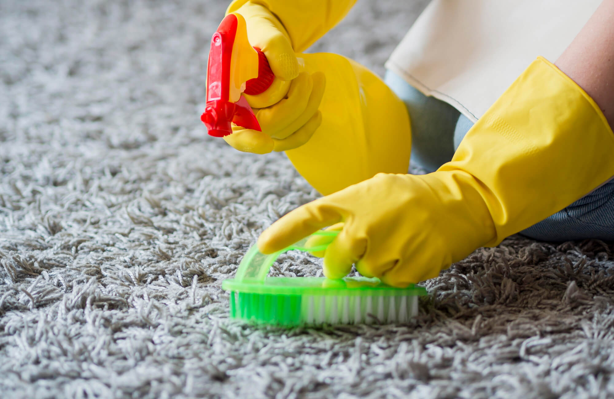 null Person wearing yellow gloves scrubbing a gray polypropylene shag rug with a brush and spray cleaner, ensuring a deep and thorough clean.