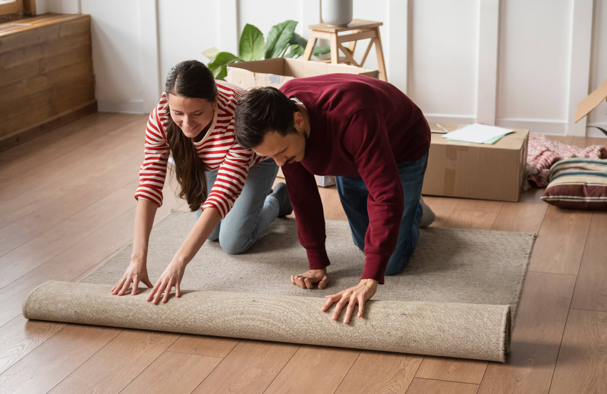 null Smiling couple rolling out a polypropylene area rug in their new home, adding warmth and comfort to the wooden flooring.