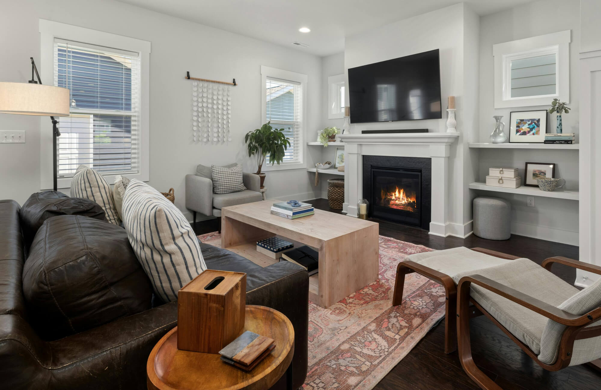 A cozy living room with a distressed rug in muted pink and beige tones beneath a wooden coffee table, paired with a leather sofa and a lit fireplace.