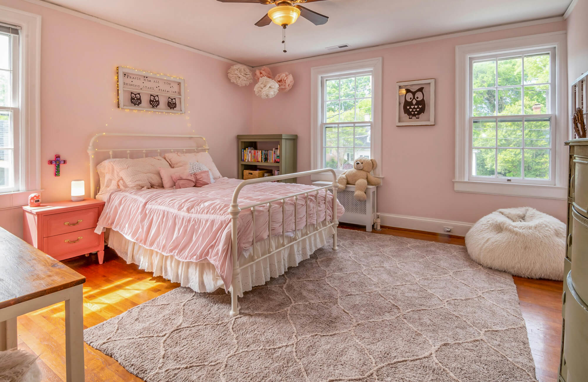 Charming pink bedroom with a white metal bed, soft ruched bedding, and a plush geometric-patterned pink rug, creating a cozy, elegant space.