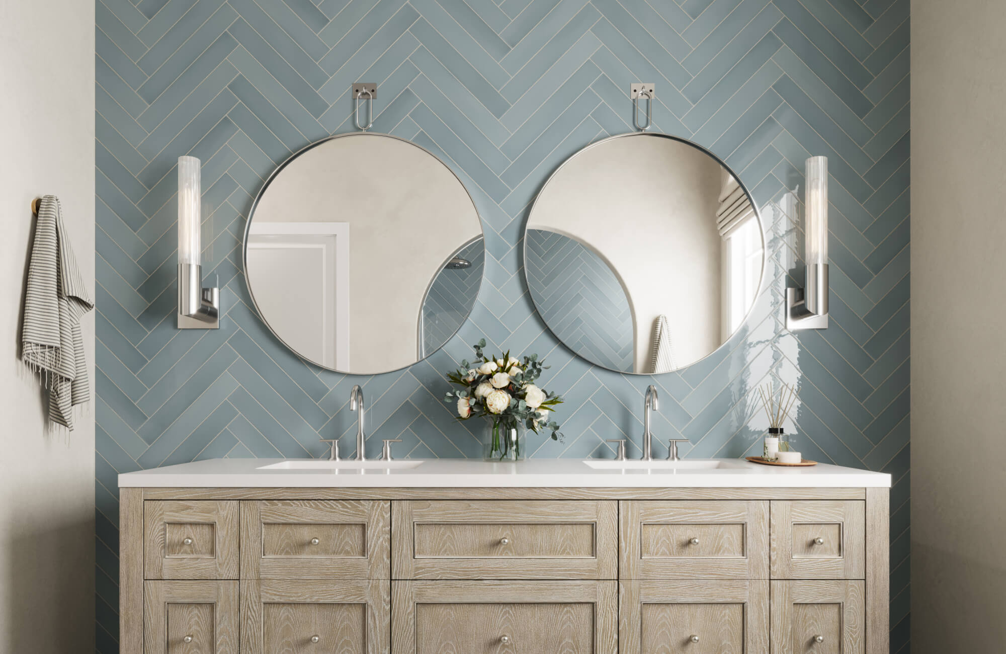 Bathroom with dual round mirrors, light wood vanity, and soft blue herringbone tiles accented by sleek chrome fixtures.