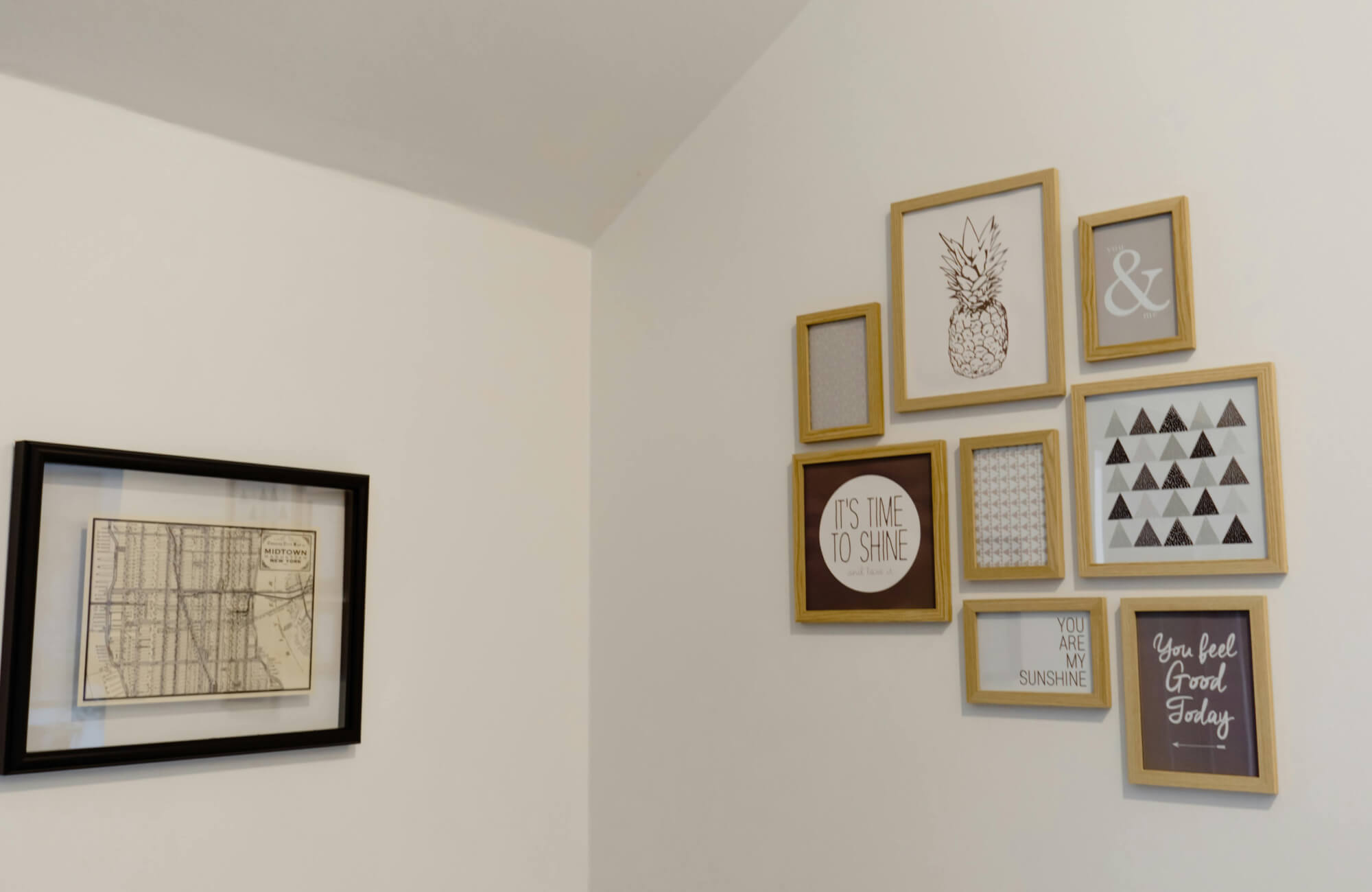 Gallery wall with light wood frames in beige, brown, and gray tones, arranged in a tight cluster to build visual height and scale on a tall white wall.