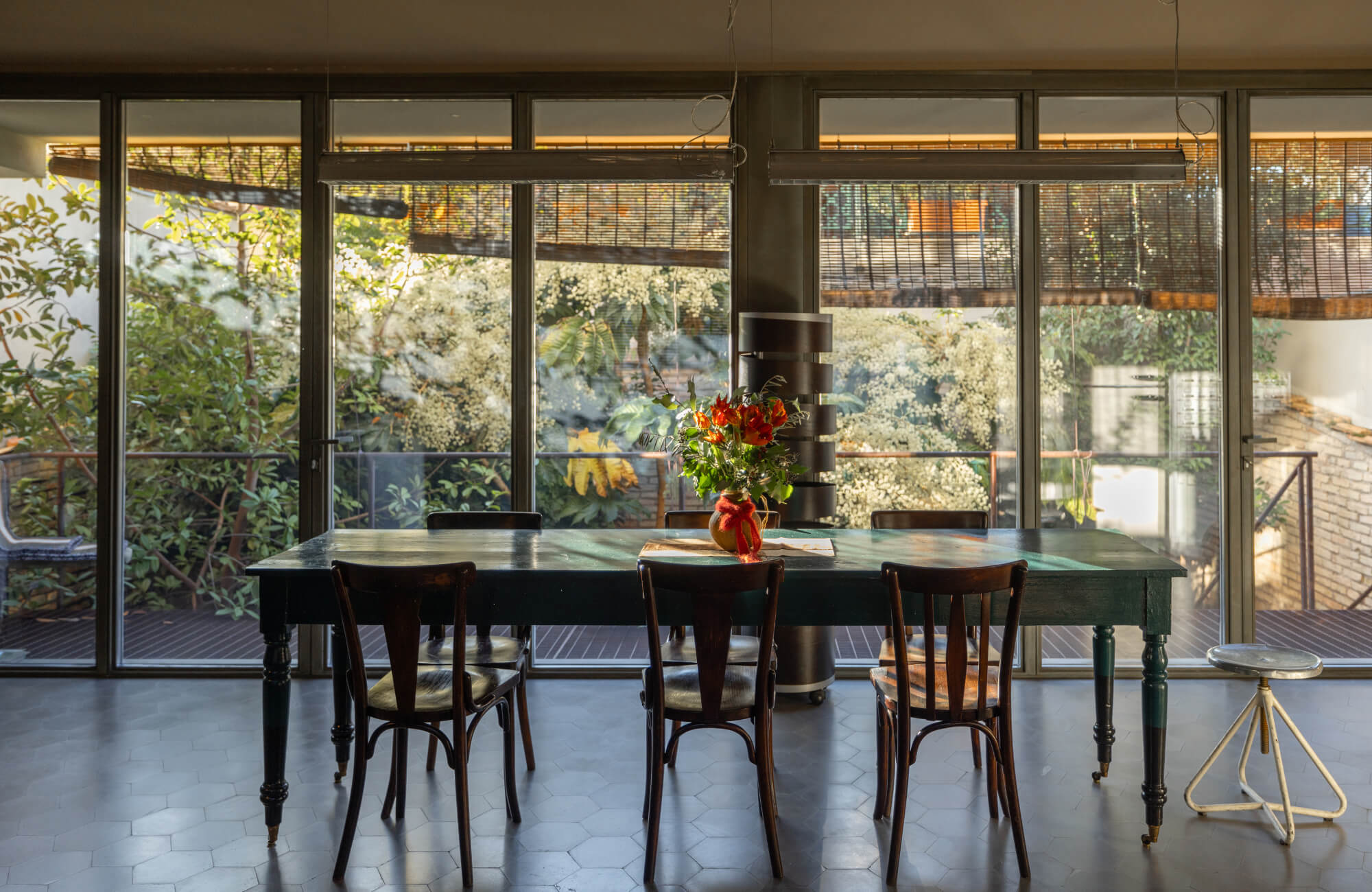 Dark wood rectangular dining table styled simply with a floral centerpiece, surrounded by classic chairs and large glass windows.