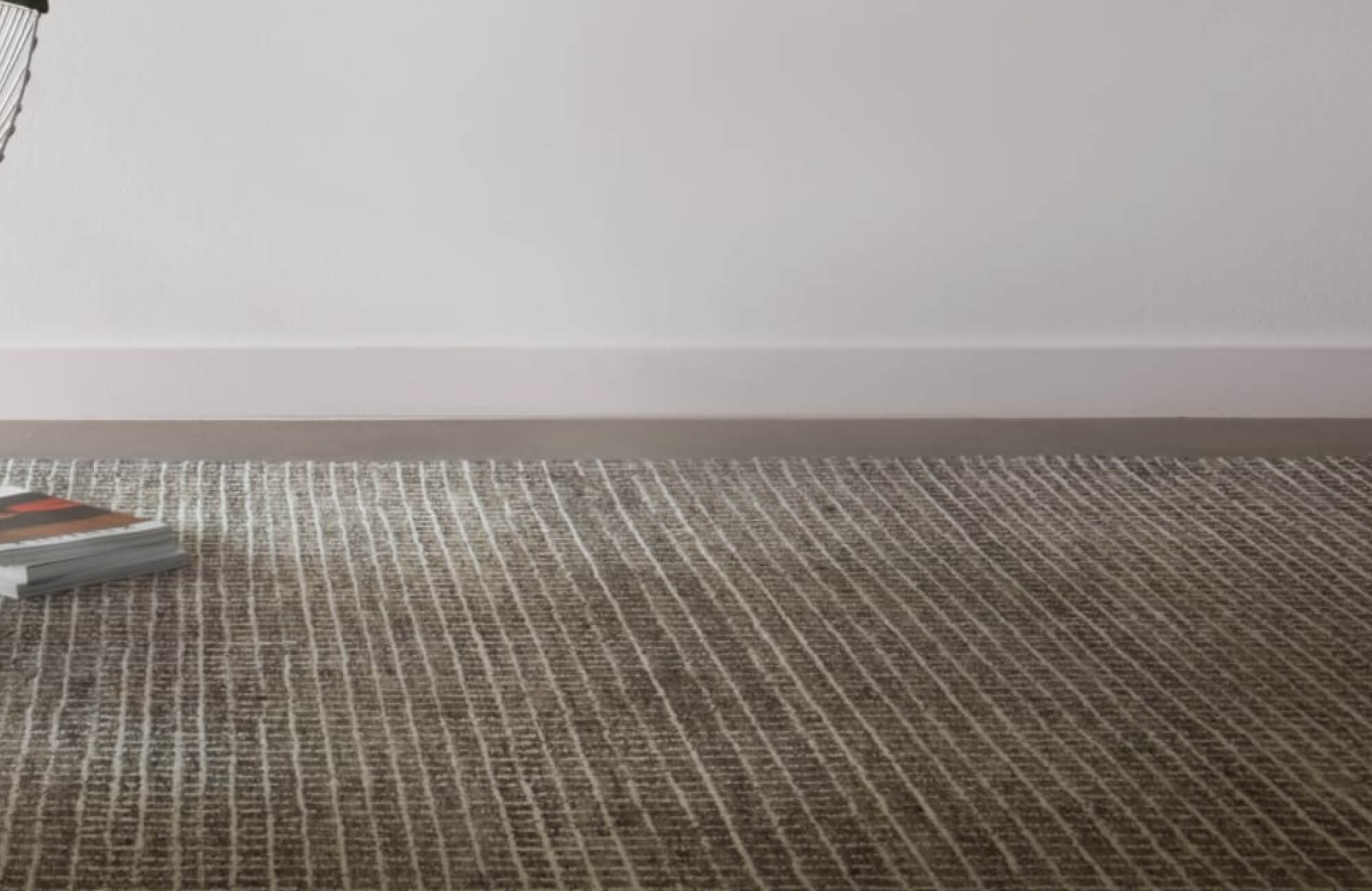 null Modern space with a charcoal grid-pattern wool rug, bordered by white walls and a stack of magazines in the corner.