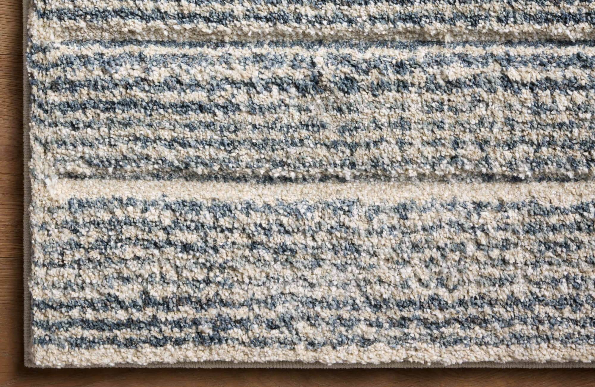 null Layered polypropylene rug in soft cream and blue stripes, showcasing plush texture atop a wood floor.