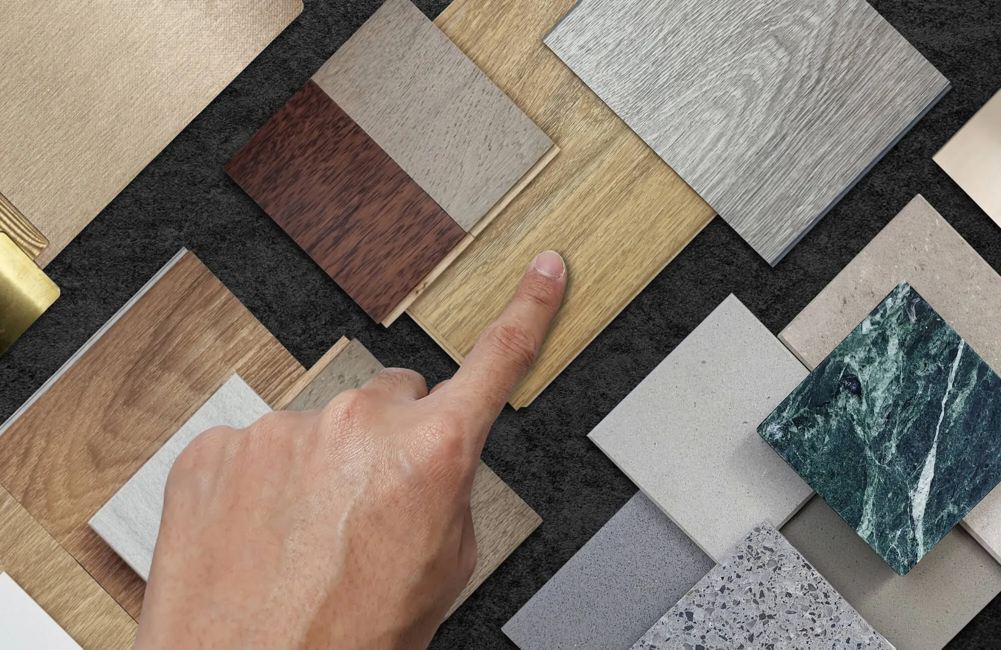 Hand selecting wood and tile samples, comparing oak planks with marble-look tiles and neutral finishes on a textured surface.