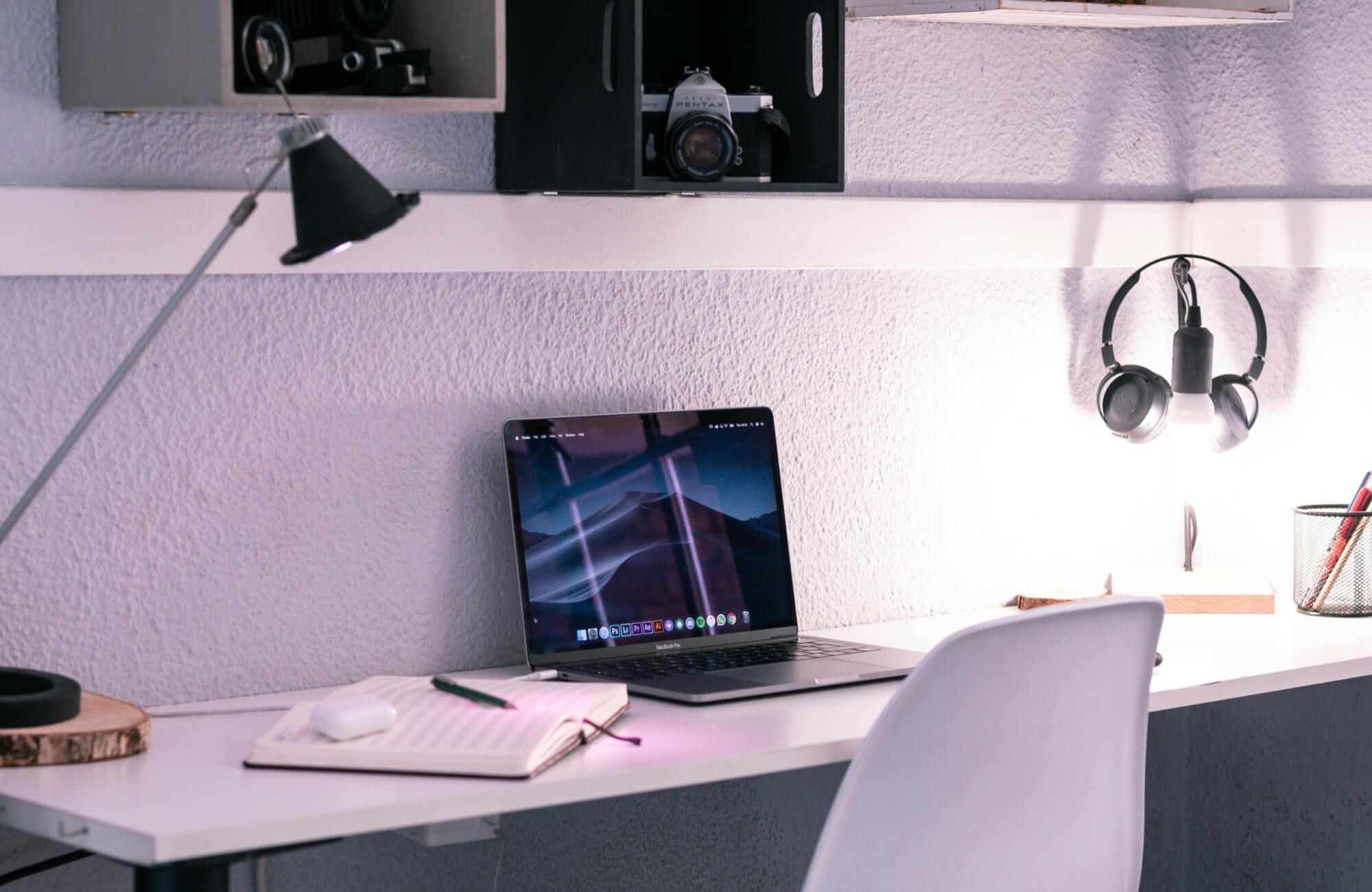 Minimalist home workspace with a laptop, open notebook, and task lighting against a textured white wall.