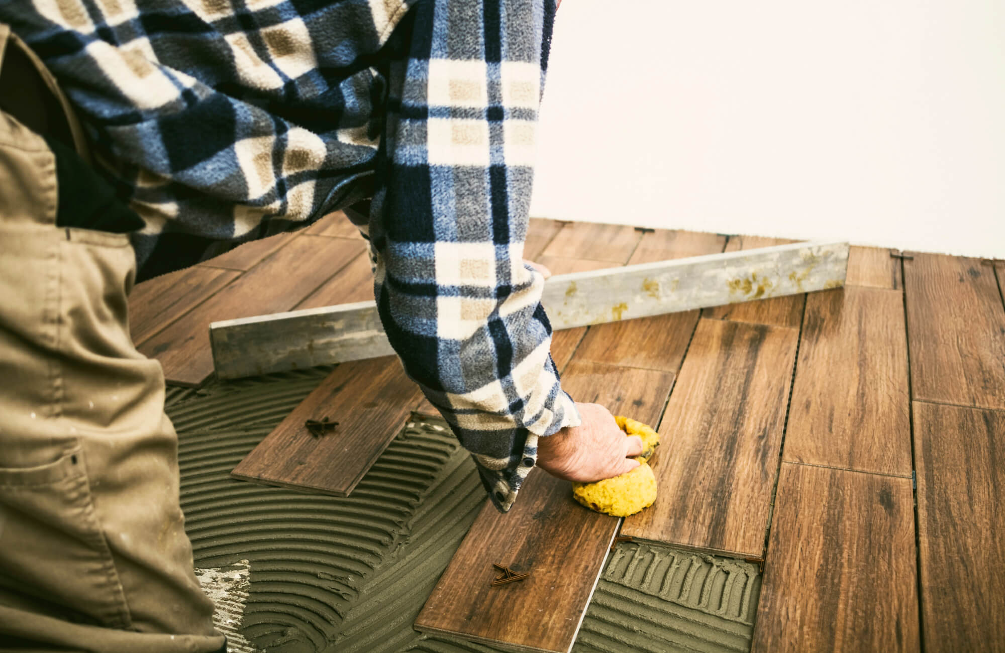 null Close-up of a worker installing wood look tile over mortar with spacers and a sponge, showing detailed flooring technique and texture.