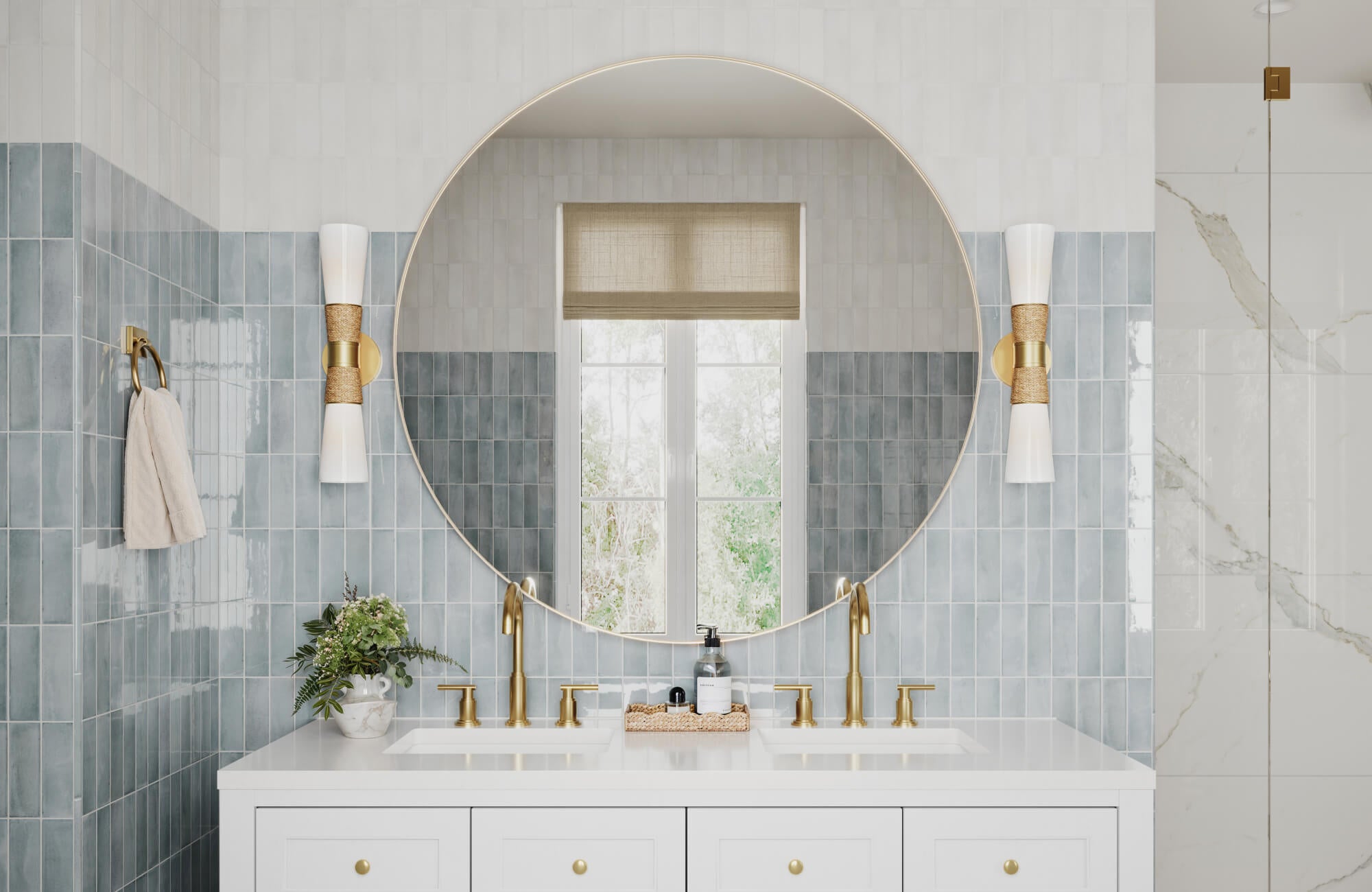 null White vanity with gold fixtures, soft blue vertical tile, and a large round mirror reflecting a window view.