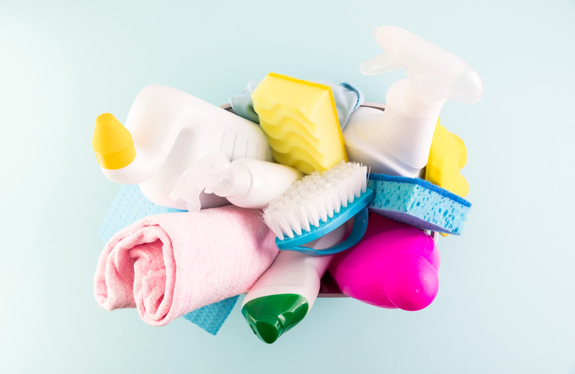 A bucket filled with assorted cleaning supplies, including spray bottles, sponges, a scrub brush, and folded microfiber cloths.