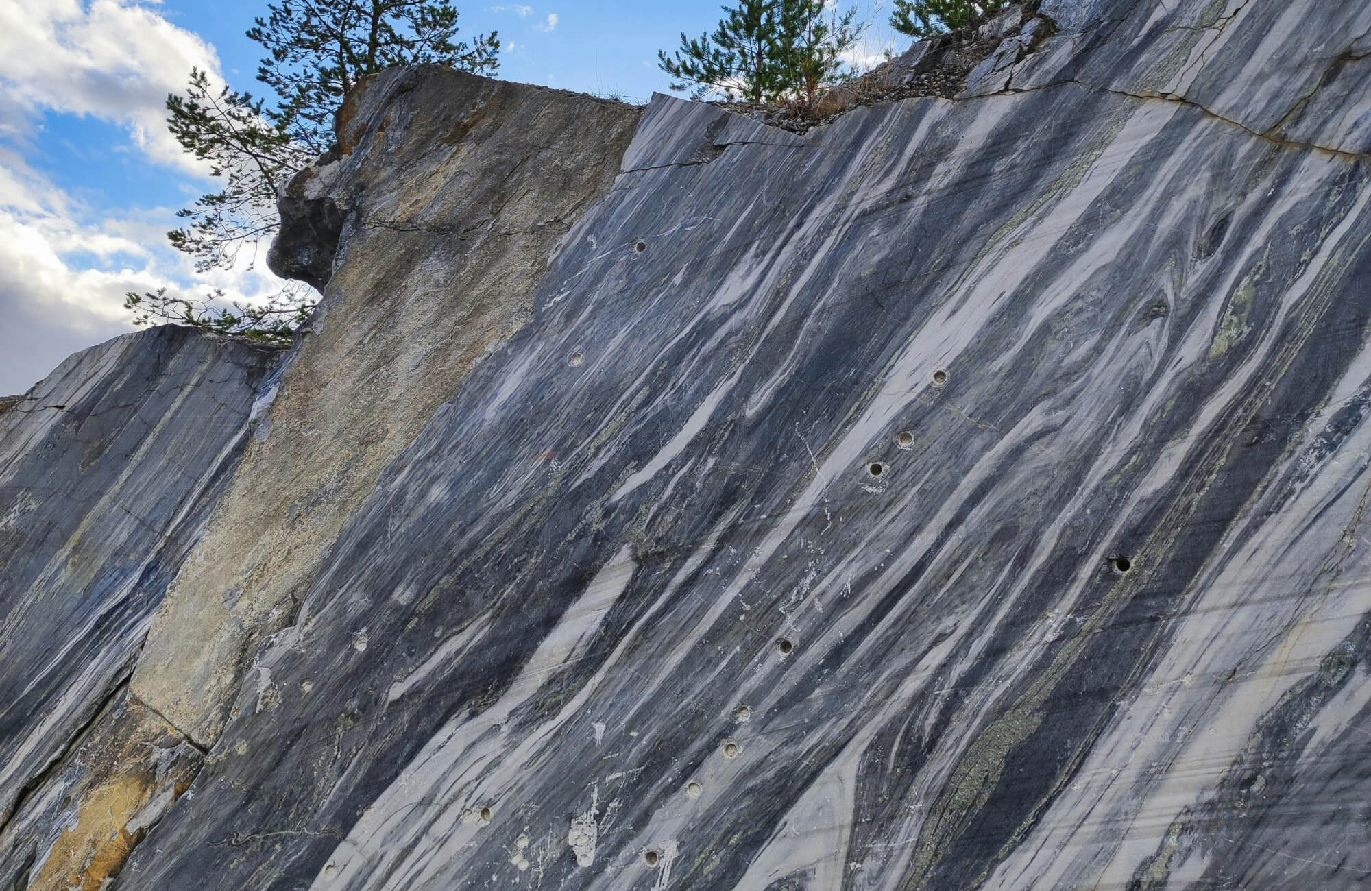 null Close-up of a dramatic marble quarry wall featuring bold grey and white veining with visible drill marks.