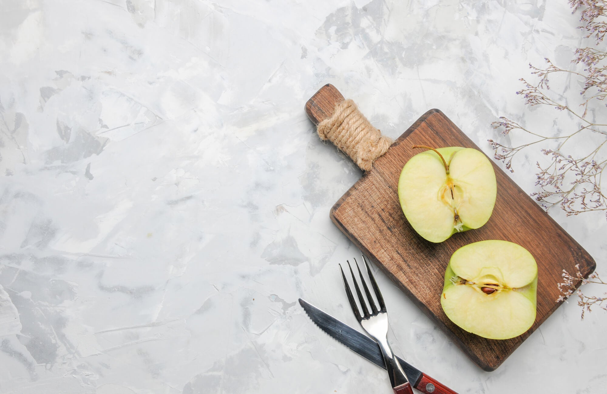 null Marble countertop with a wooden cutting board holding a sliced green apple, alongside a fork and knife.