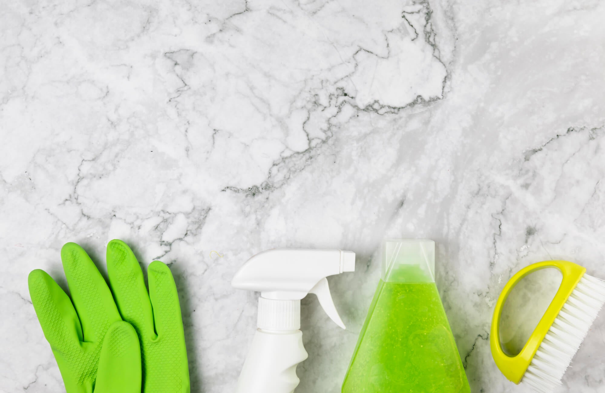 null Marble countertop with green cleaning gloves, a spray bottle, a bottle of cleaner, and a scrubbing brush.