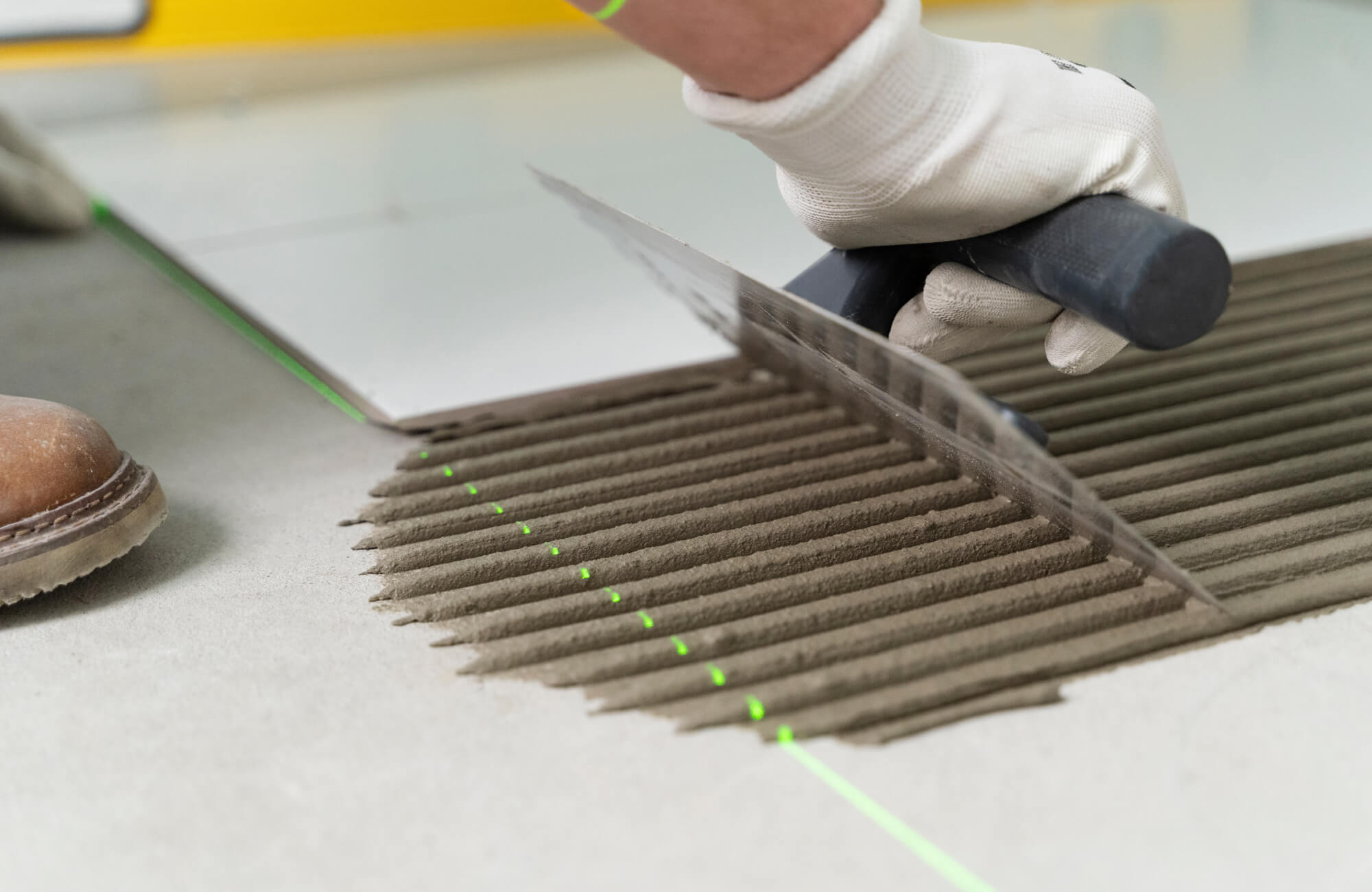 Precision troweling of adhesive mortar in progress during a porcelain tile installation using laser-guided alignment.