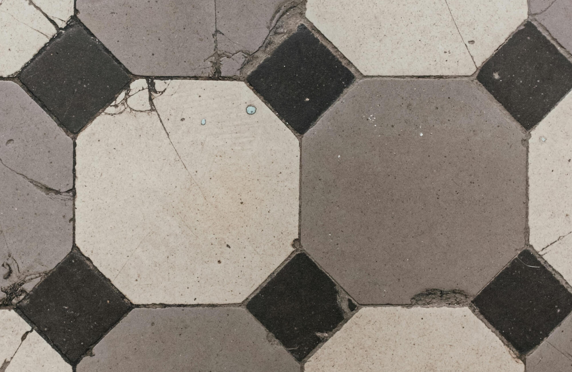 Cracked porcelain tile layout with an aged octagon-and-dot pattern in beige, gray, and black tones.