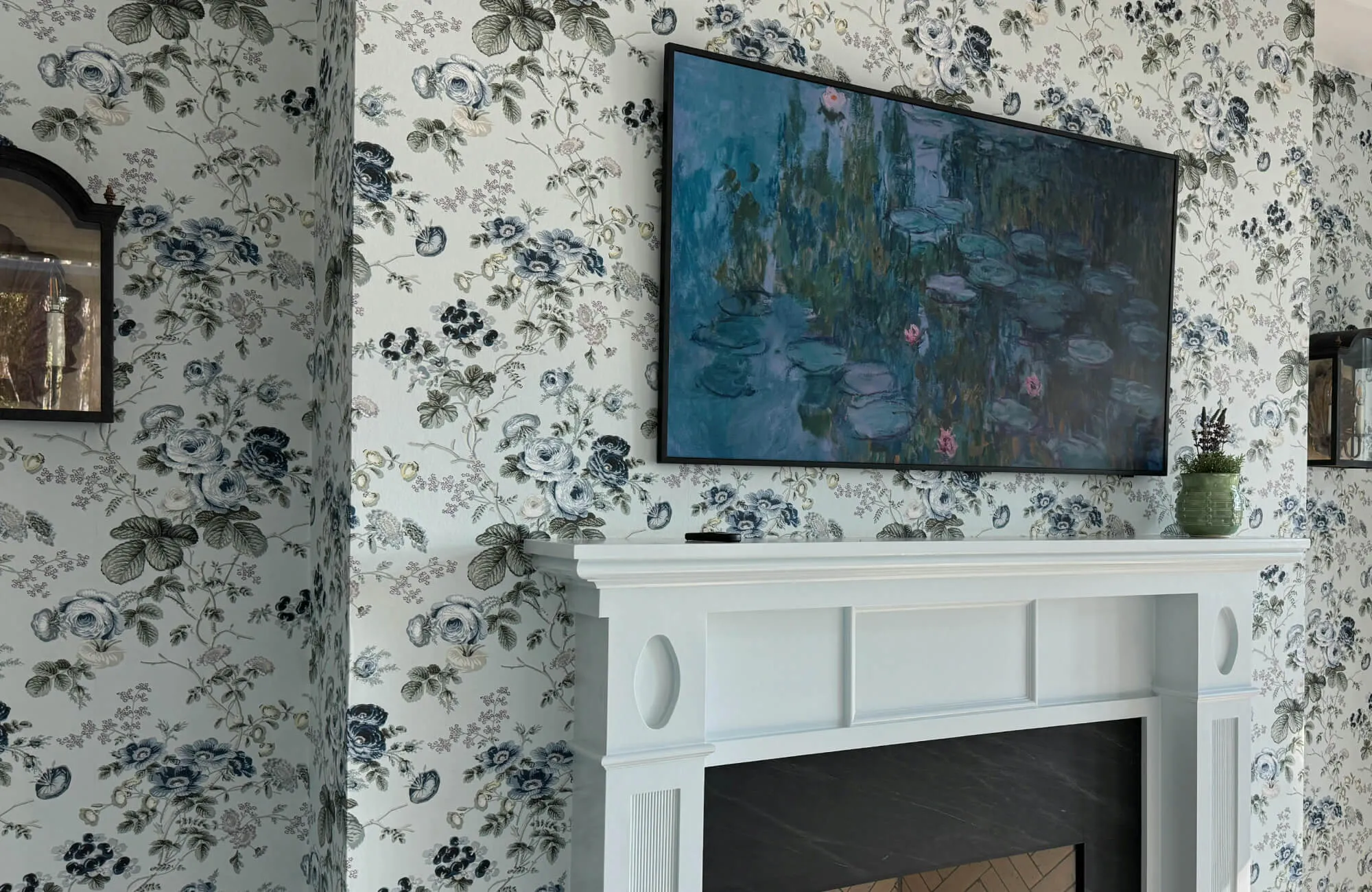 Peel and stick wallpaper with blue floral toile pattern styled behind a wall-mounted TV above a white fireplace mantel.