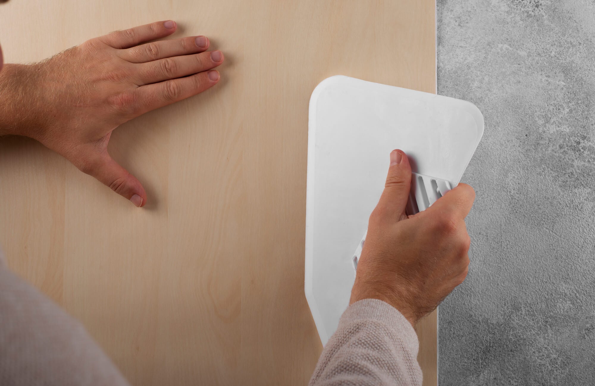 null Peel and stick wallpaper being smoothed with a plastic scraper during installation on a wall surface.