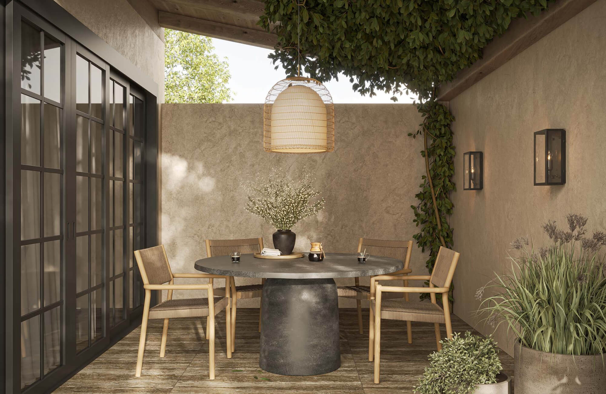 Compact covered patio with a round pedestal dining table, four wooden chairs, hanging pendant light, wall sconces, and surrounding potted greenery.