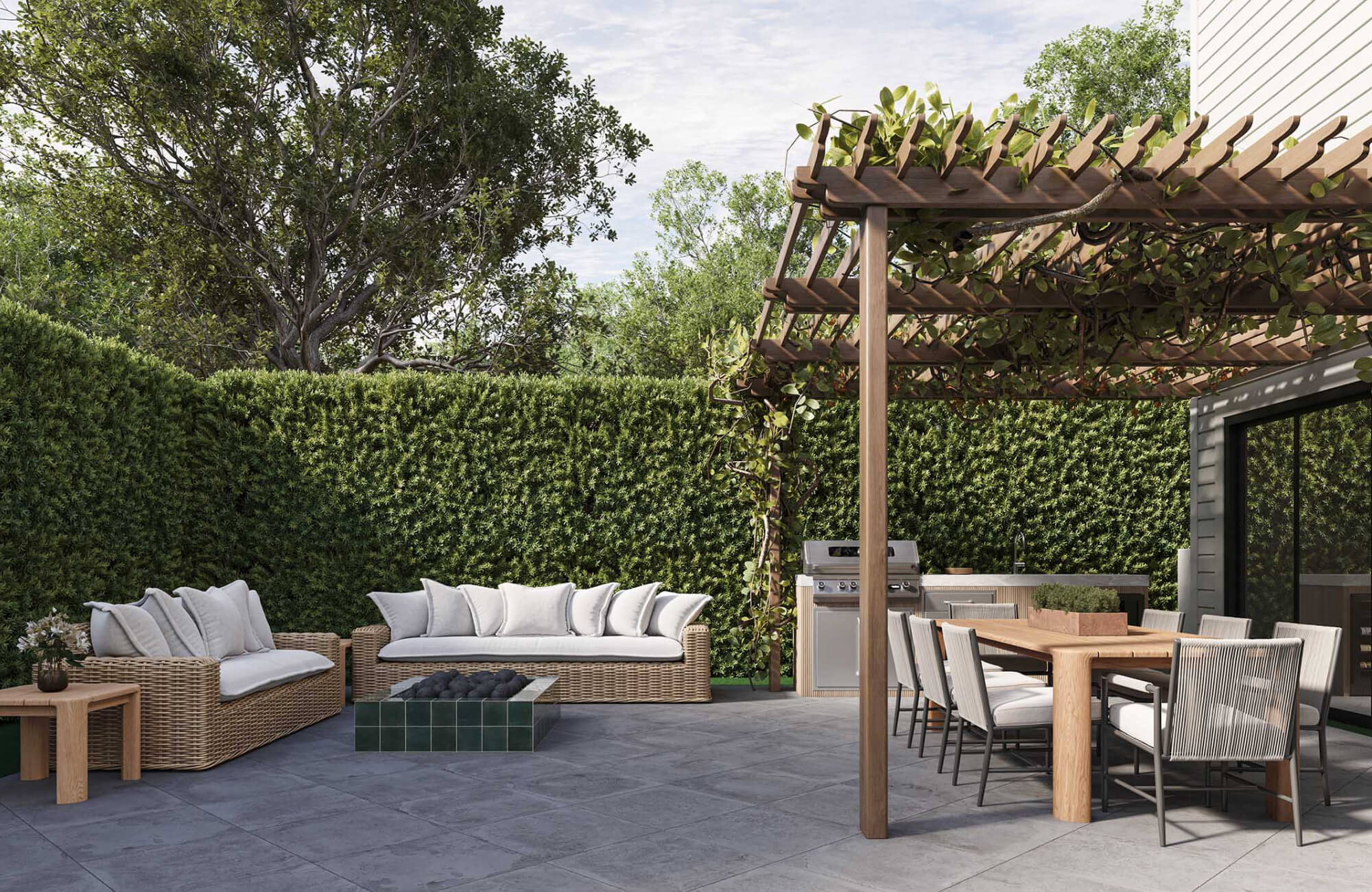 Spacious backyard patio with a long rectangular dining table under a vine-covered pergola, outdoor kitchen, lounge seating, fire feature, and tall privacy hedges.