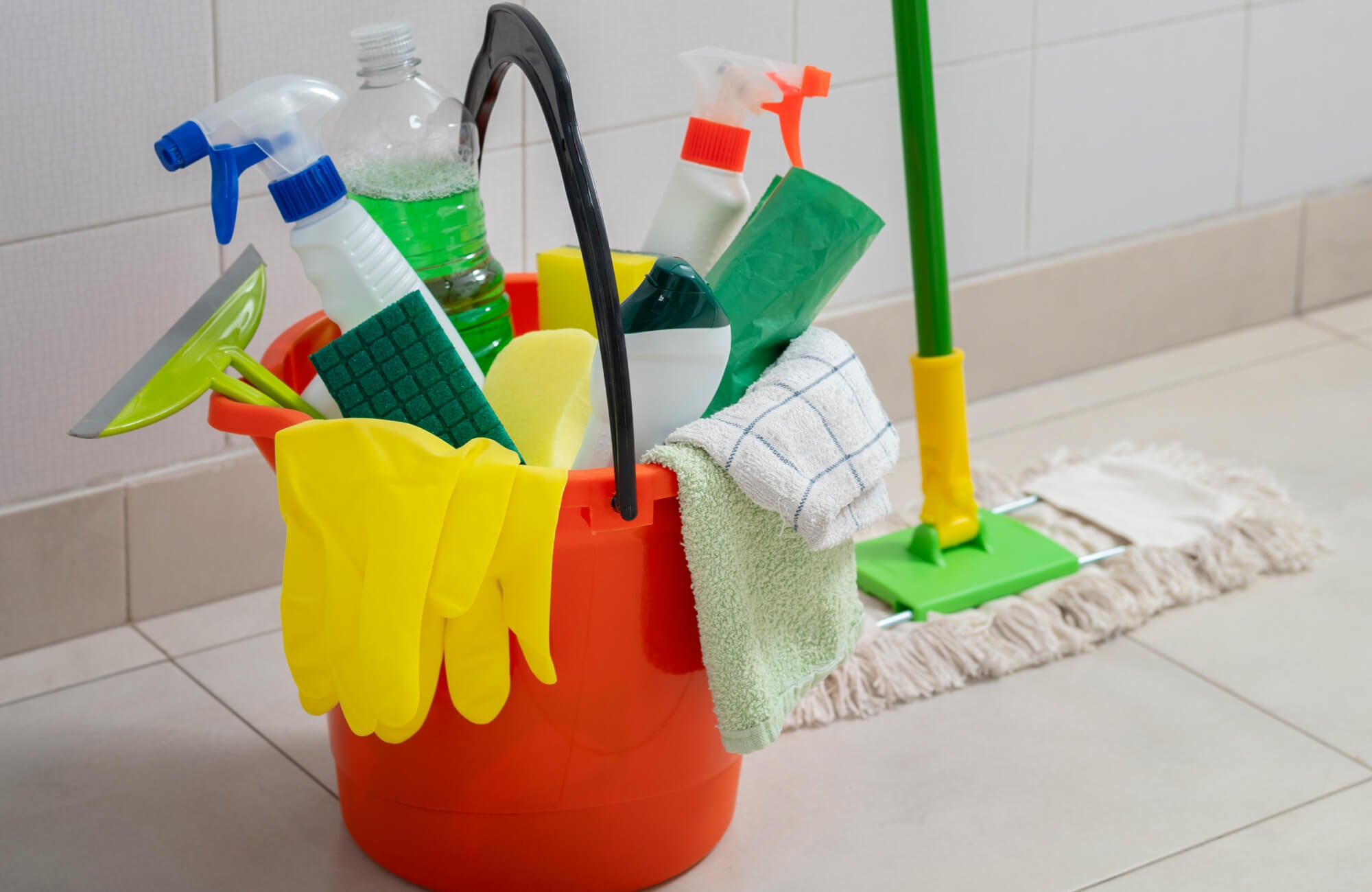 null Bright red bucket filled with cleaning supplies and gloves sits on tiled flooring, ready for a thorough surface refresh.