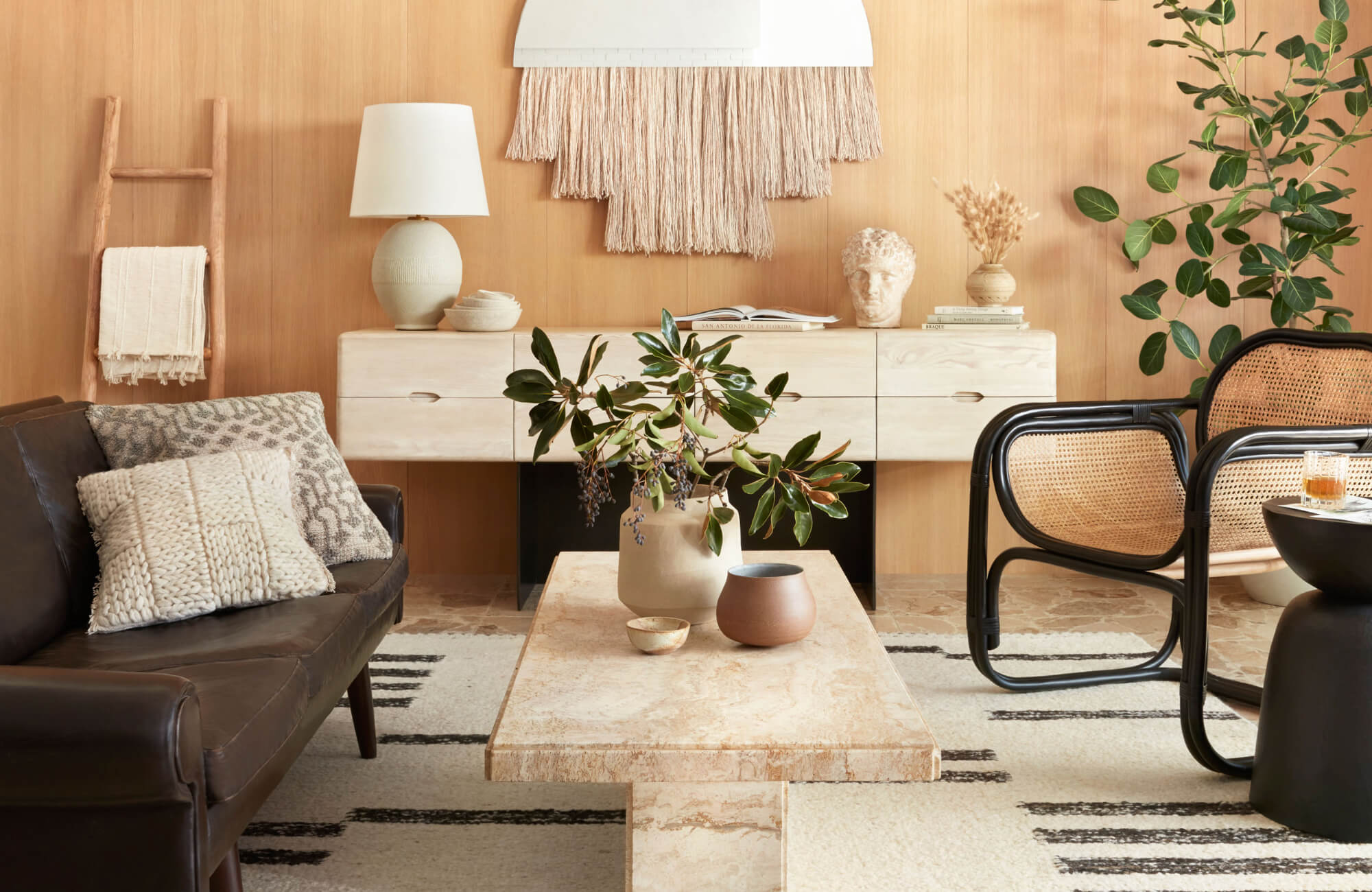 null Warm modern living room with leather sofa and textured decorative pillows beside a travertine coffee table and wood wall.