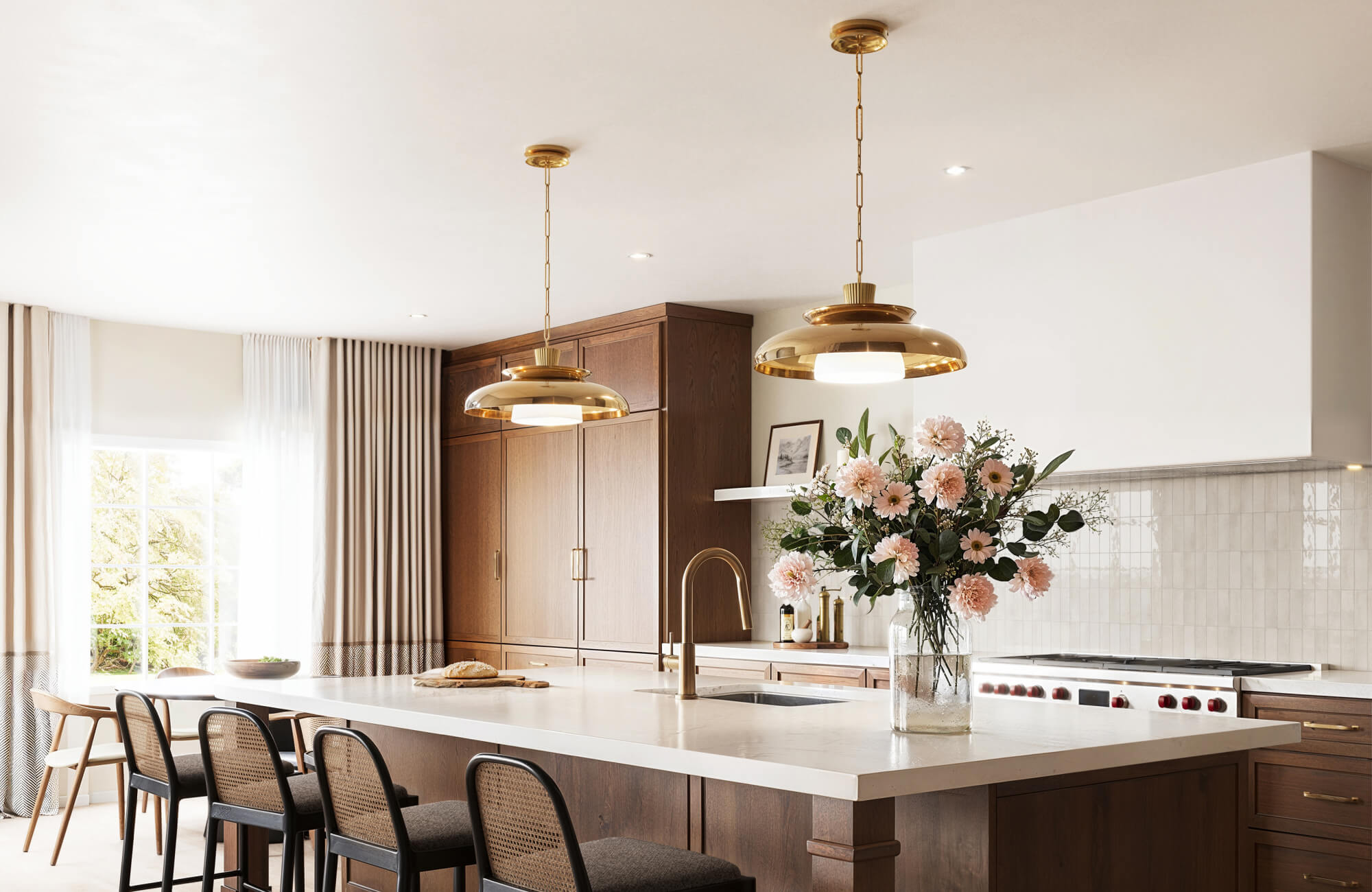 null Polished brass pendant lights shine over a spacious island, paired with warm wood cabinetry and a glossy vertical tile backsplash.