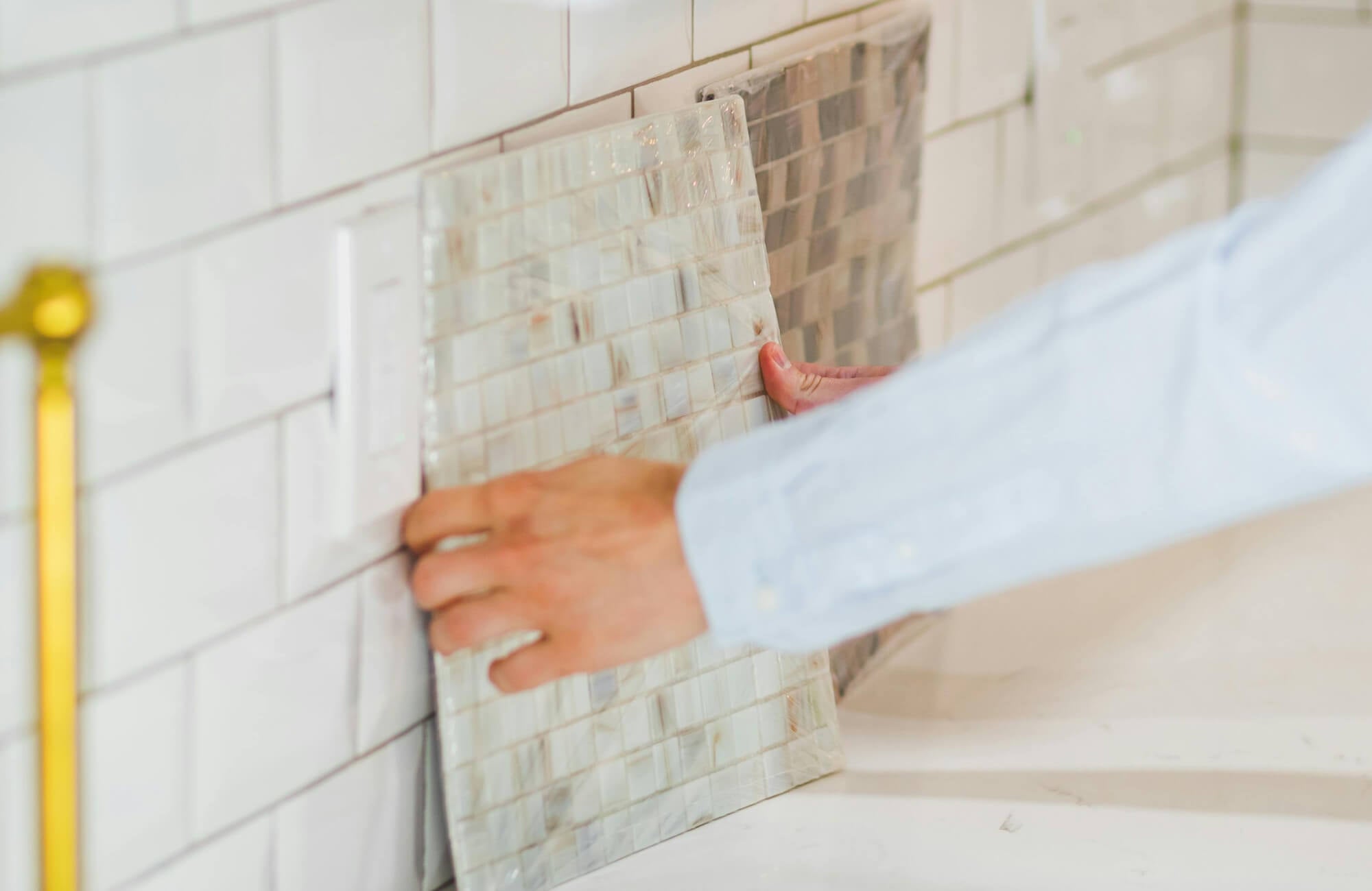 null Close-up of hands fitting new tile backsplash samples over existing subway tiles in a kitchen.