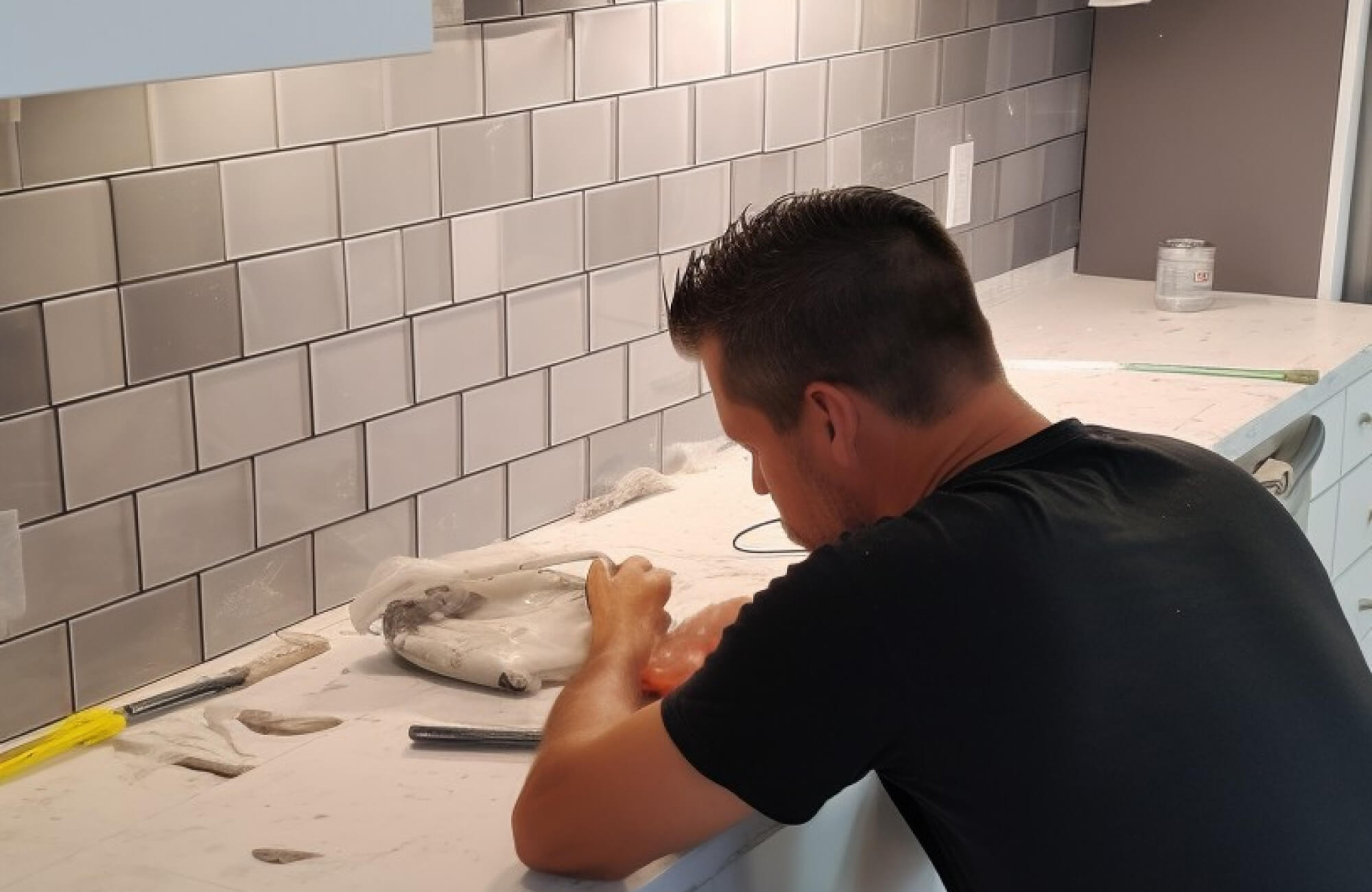 null Close-up of a worker applying grout during kitchen backsplash installation with gray subway tiles.